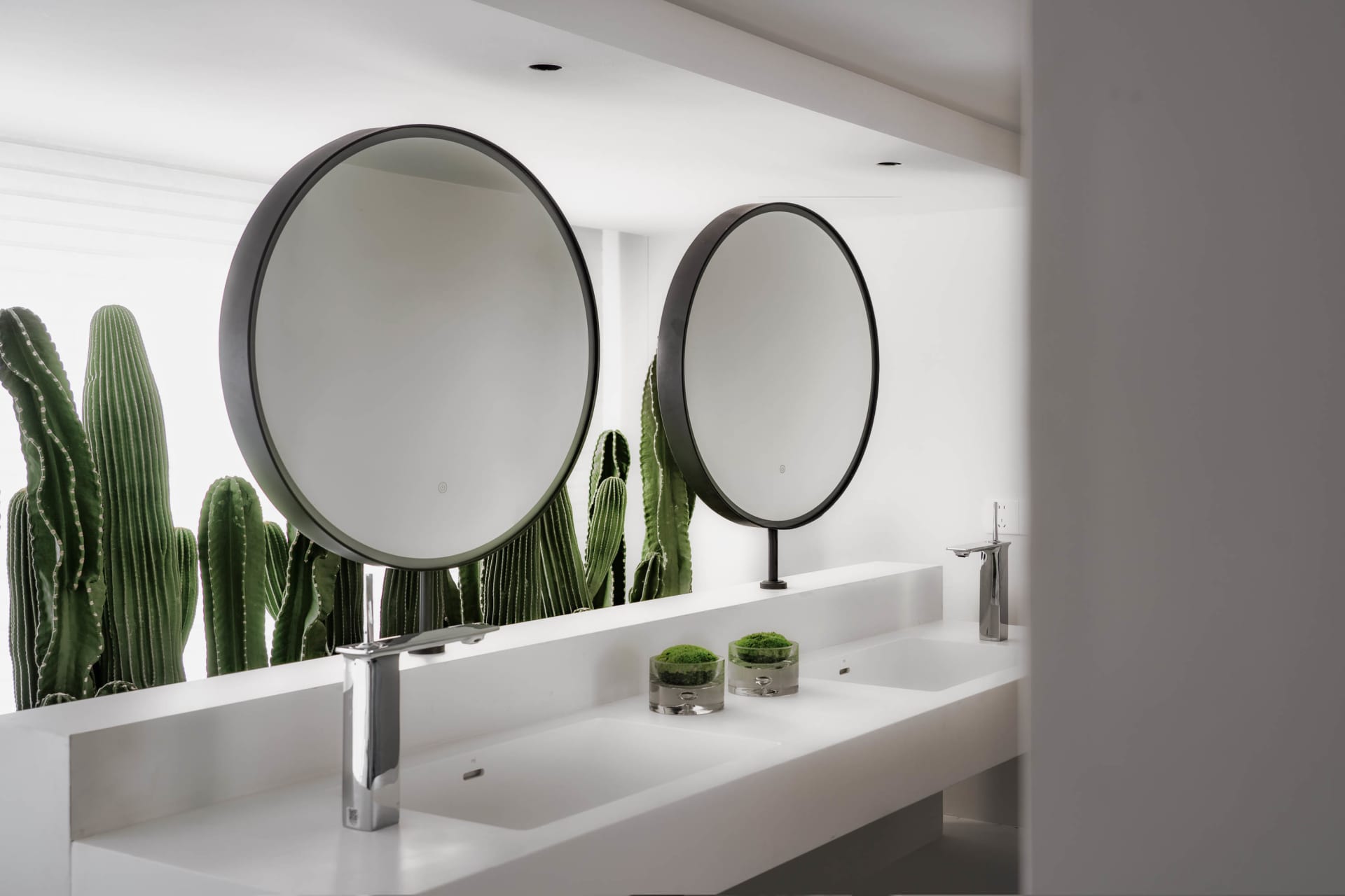 Modern minimalist bathroom with concrete countertop, white sinks, chrome faucets, and round mirrors.