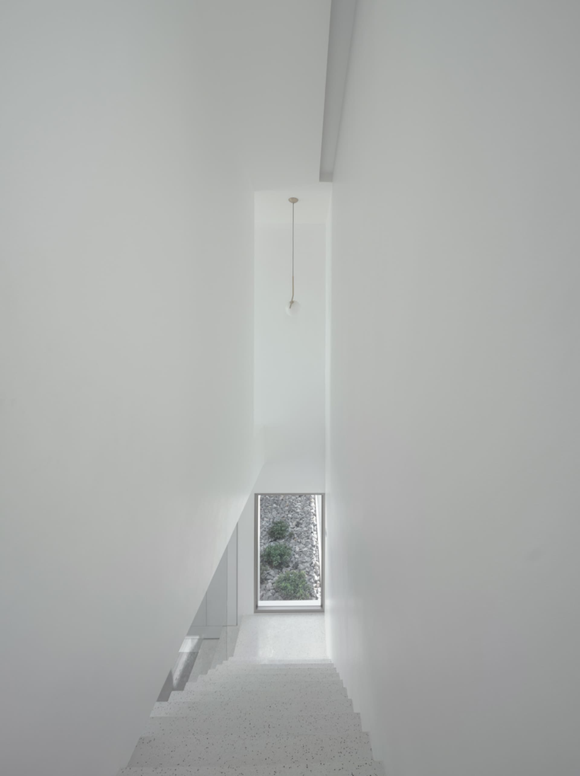 White terrazzo staircase with minimalist design leading to a window with a view of a stone garden.