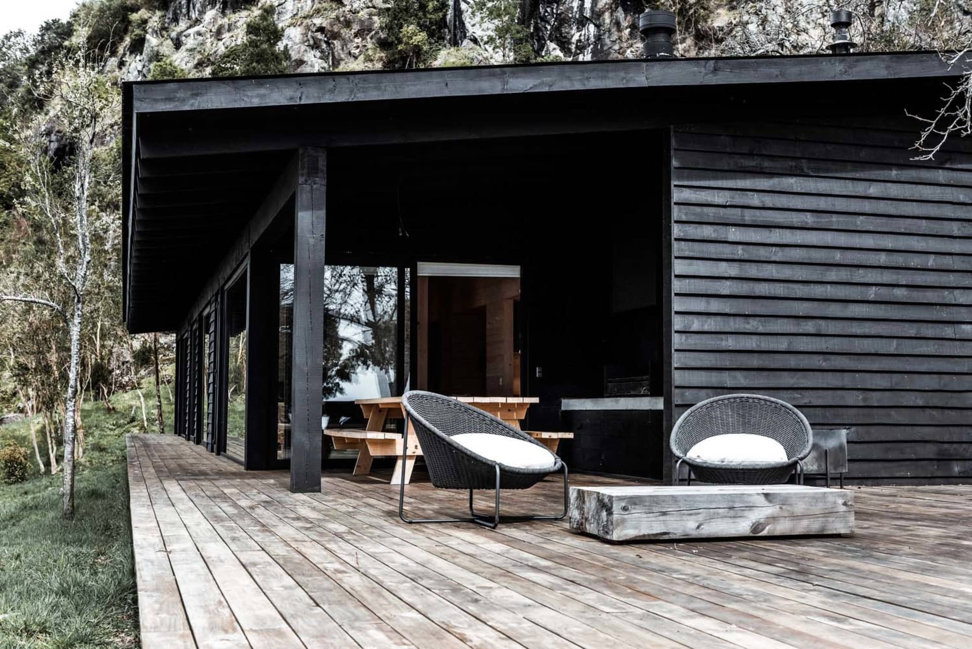 A modern black cabin with a wooden deck and white cushioned chairs.