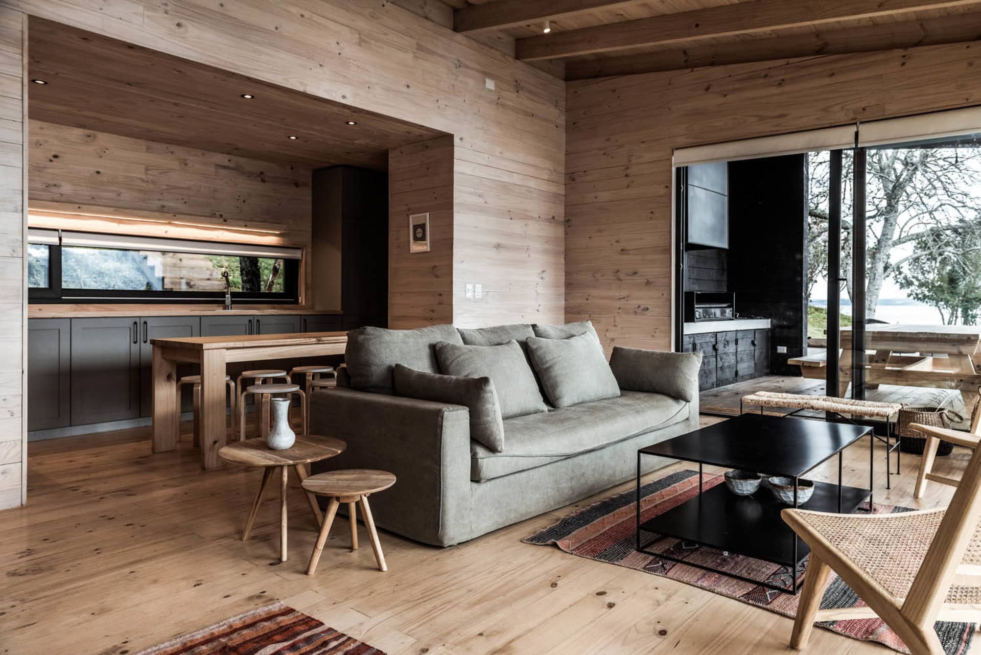 A modern Scandinavian living room featuring wooden walls and flooring, a gray sofa, and minimalistic decor.