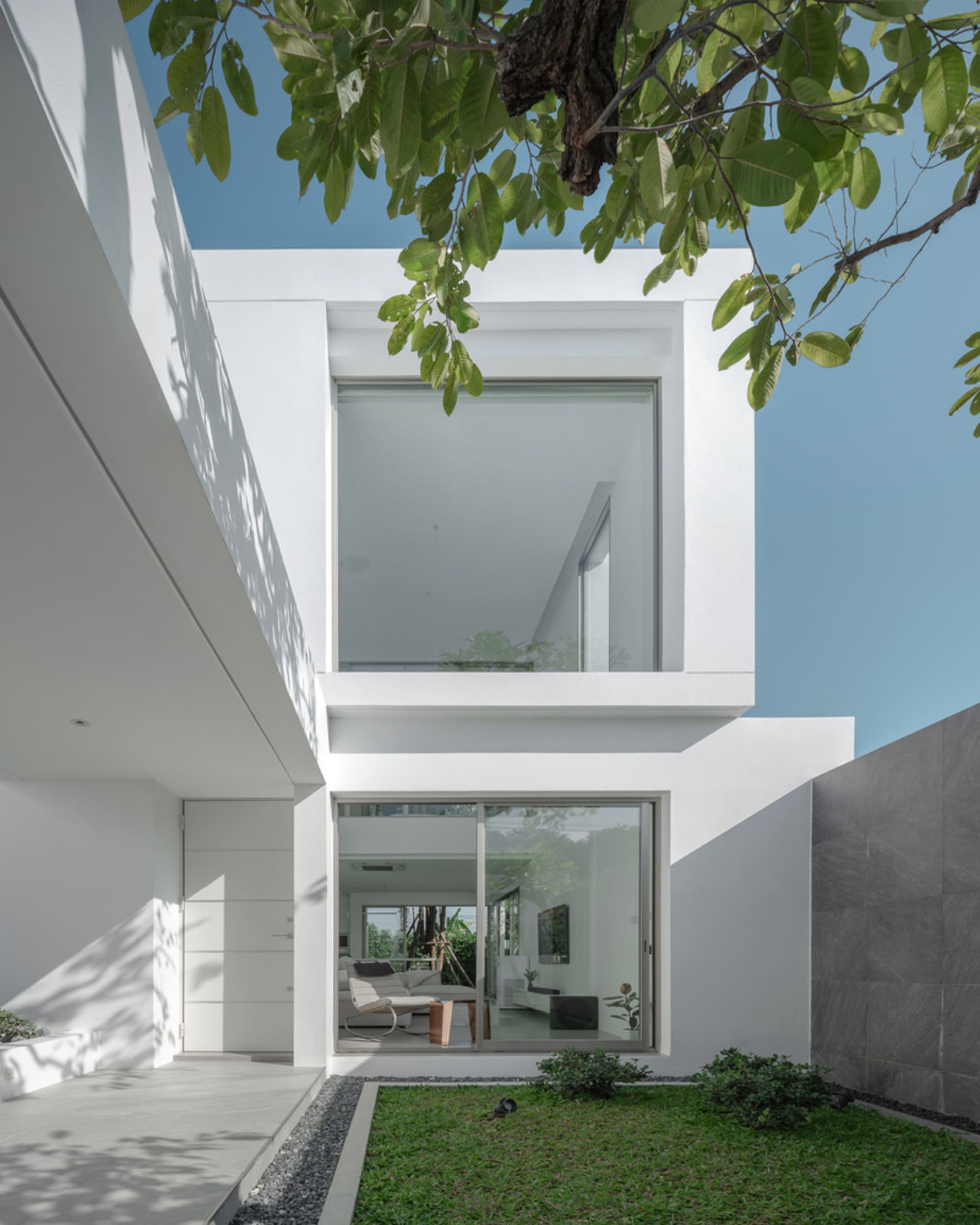 Modern minimalist white concrete house with large glass windows and greenery.