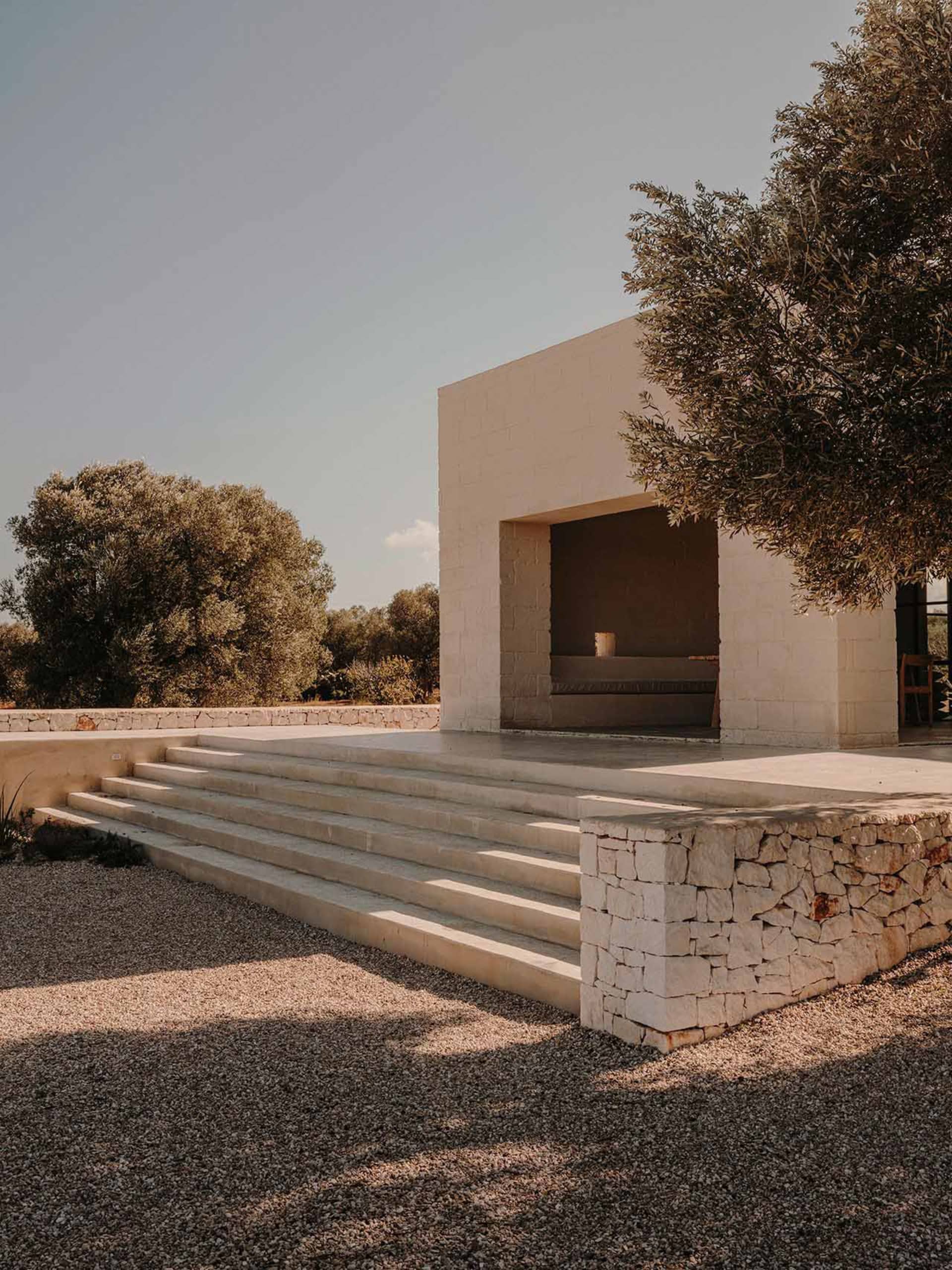 A modern architectural space with a concrete exterior, featuring a central open area surrounded by a stone wall and steps lea