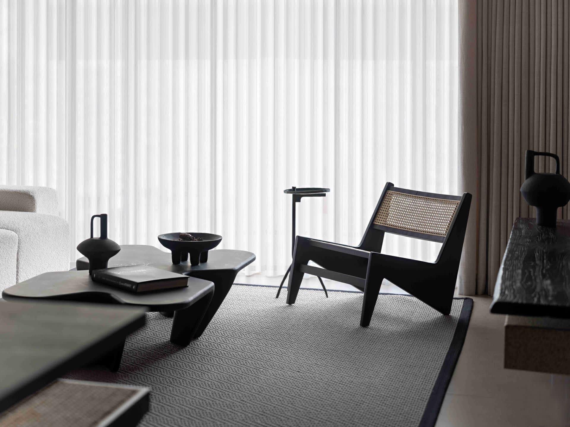 Modern minimalist living room with black furniture, white curtains, and a textured rug.