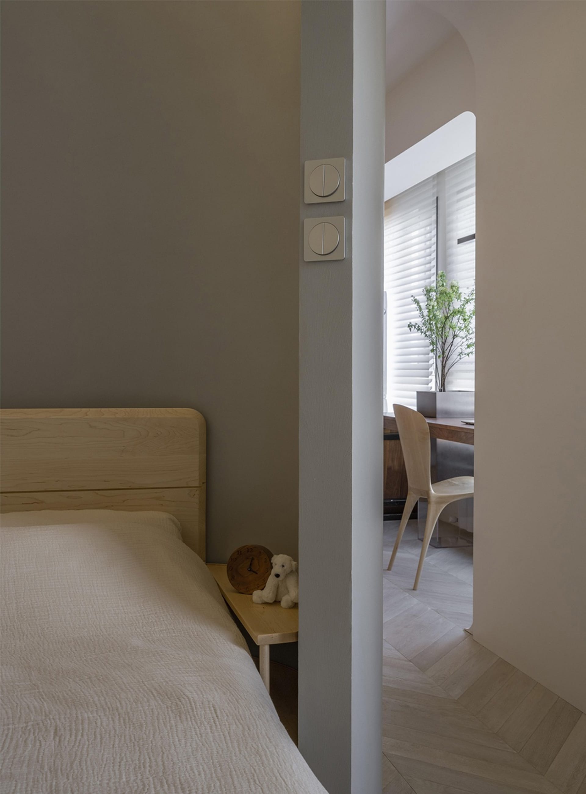 A minimalist bedroom featuring a wooden nightstand with a clock and a stuffed animal.