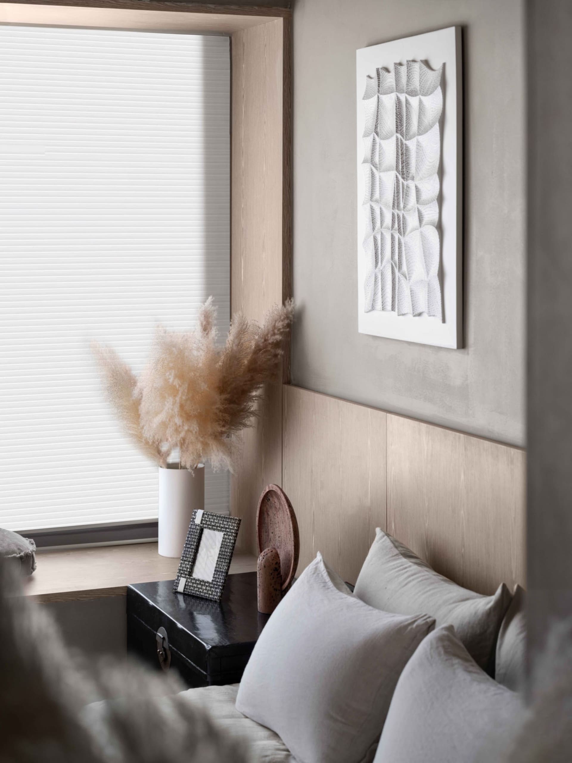 Neutral-toned minimalist interior with white and beige decor, featuring a textured abstract wall art piece and a cozy seating
