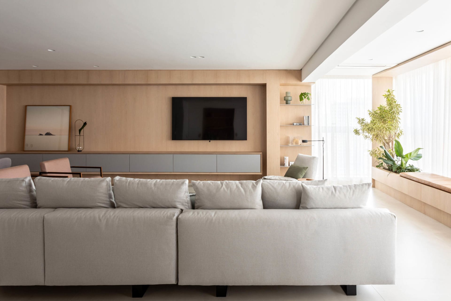 A modern minimalist living room featuring wooden furniture and a large window with plants.