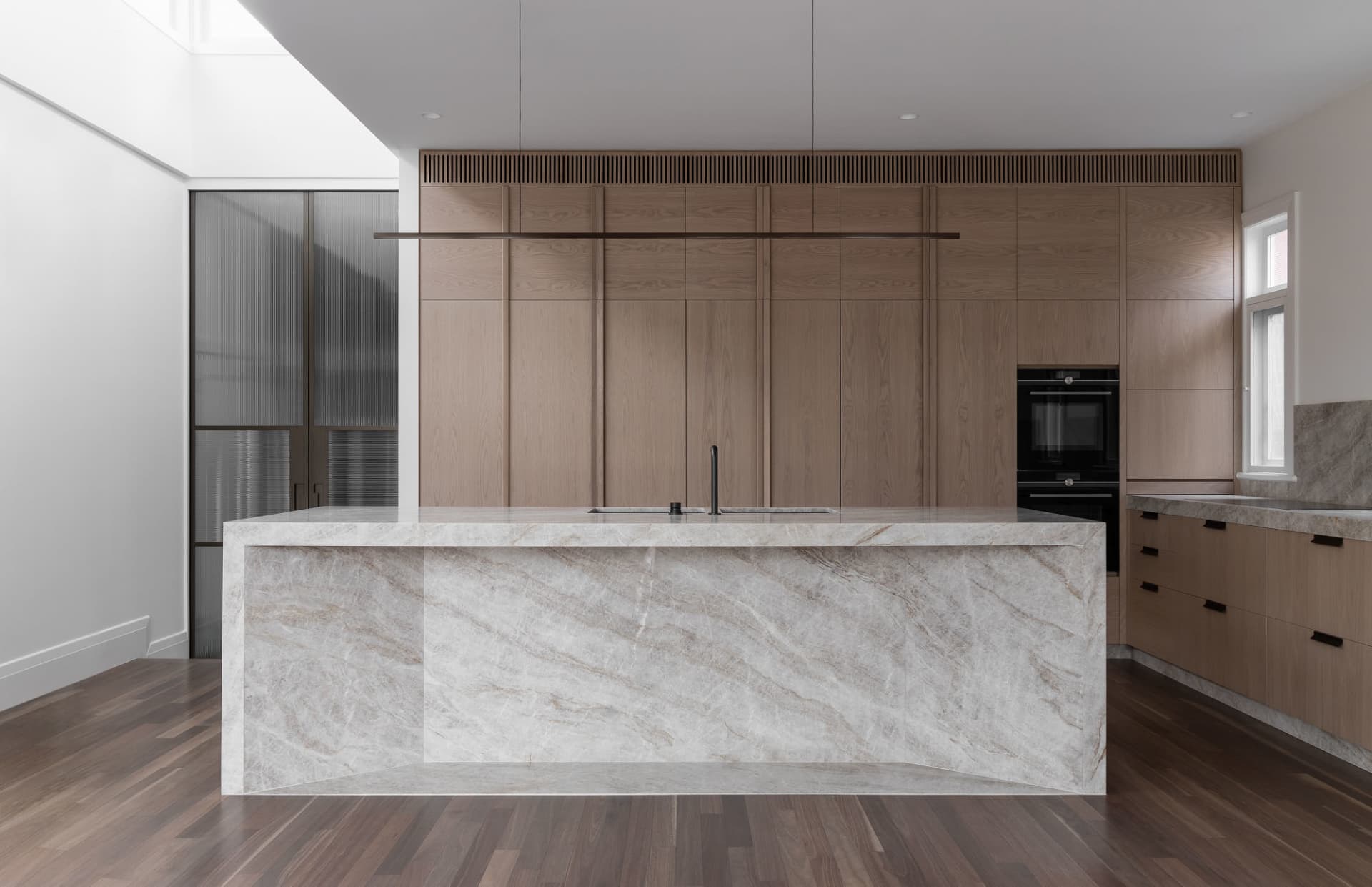 A modern kitchen featuring marble countertops and wooden cabinets.