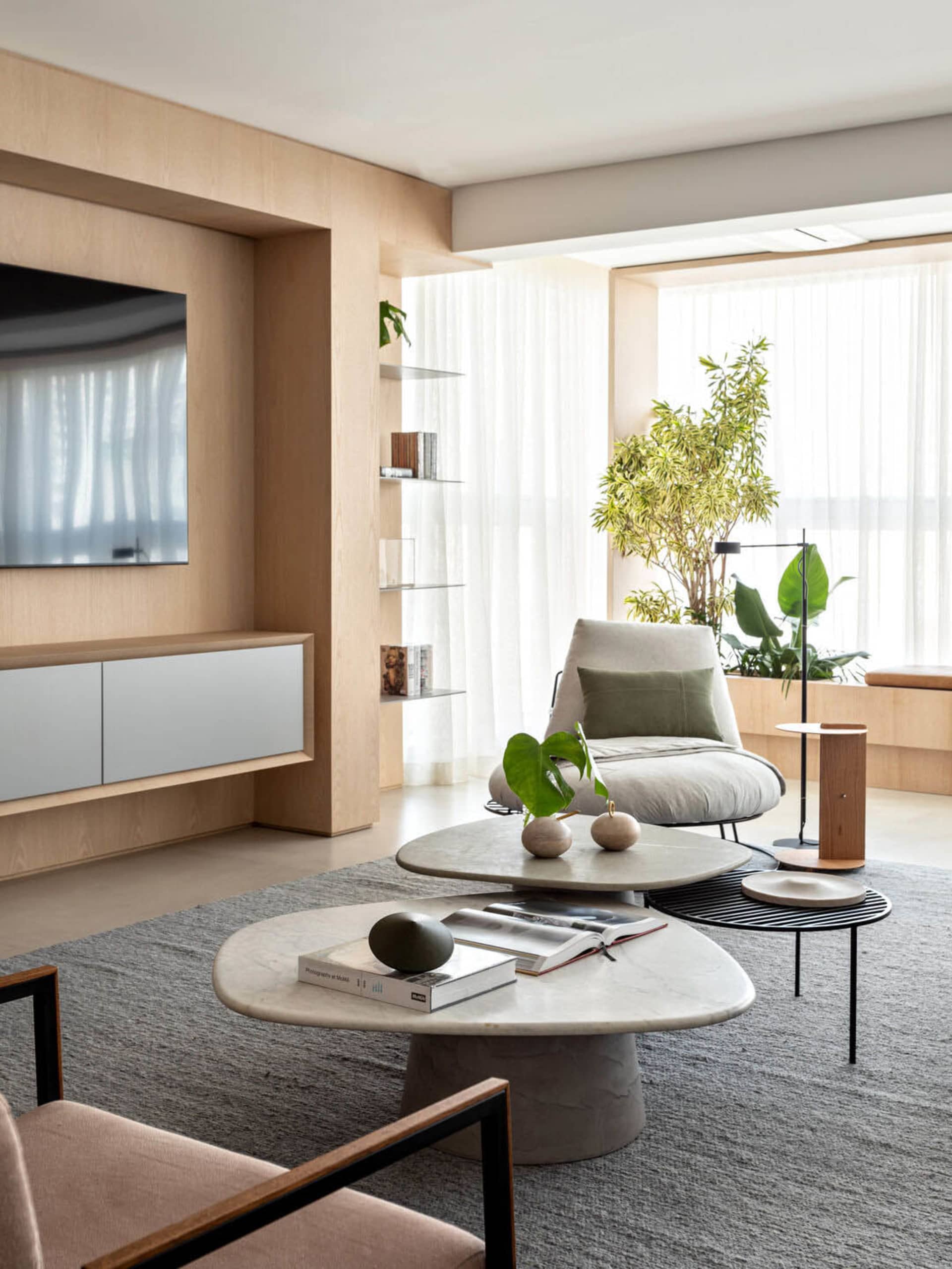 Contemporary living room with a marble coffee table, wooden armchairs, and floor-to-ceiling windows.