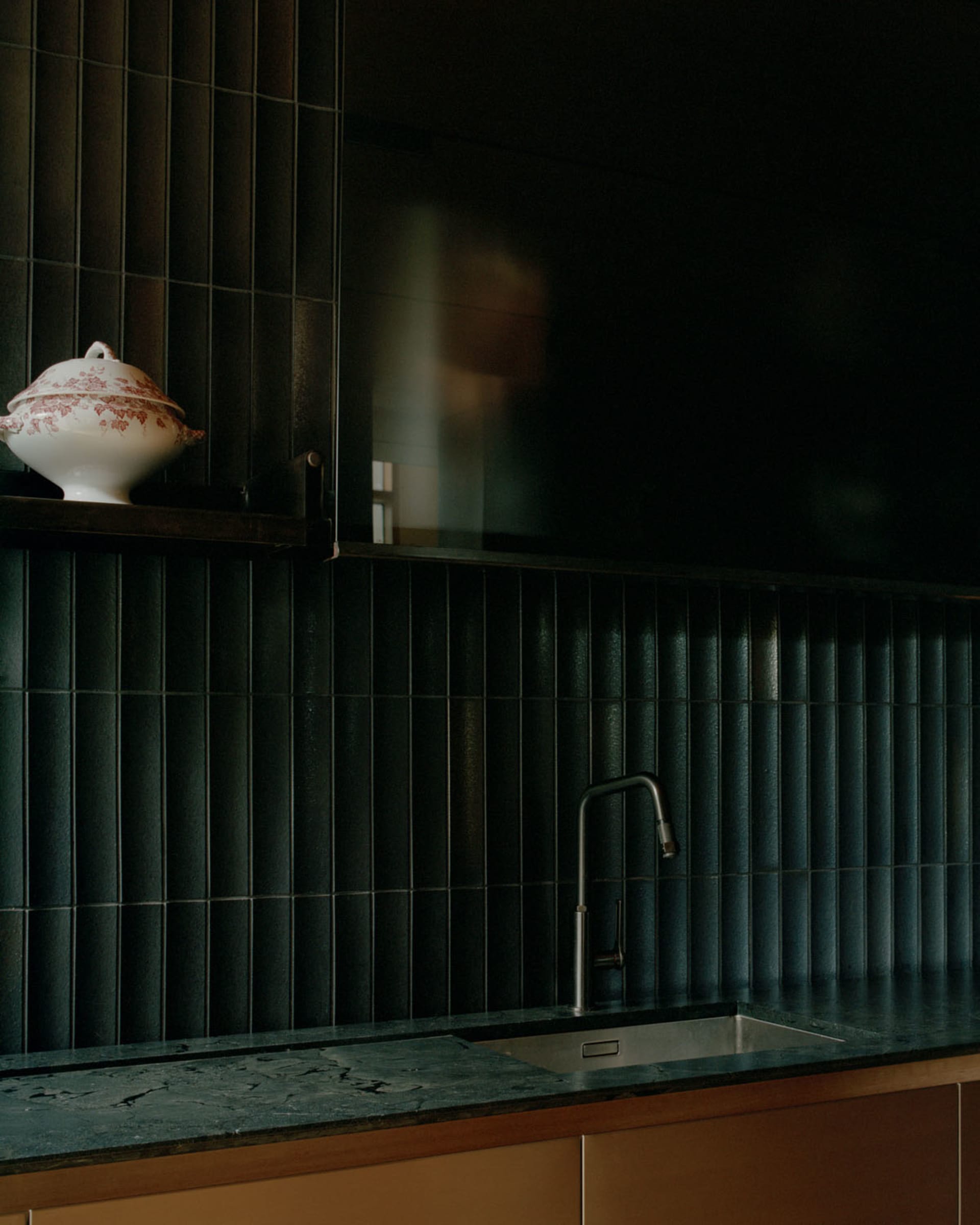 A well-equipped kitchen with marble countertops and a sink, featuring sleek black tiles and a decorative ceramic dish.