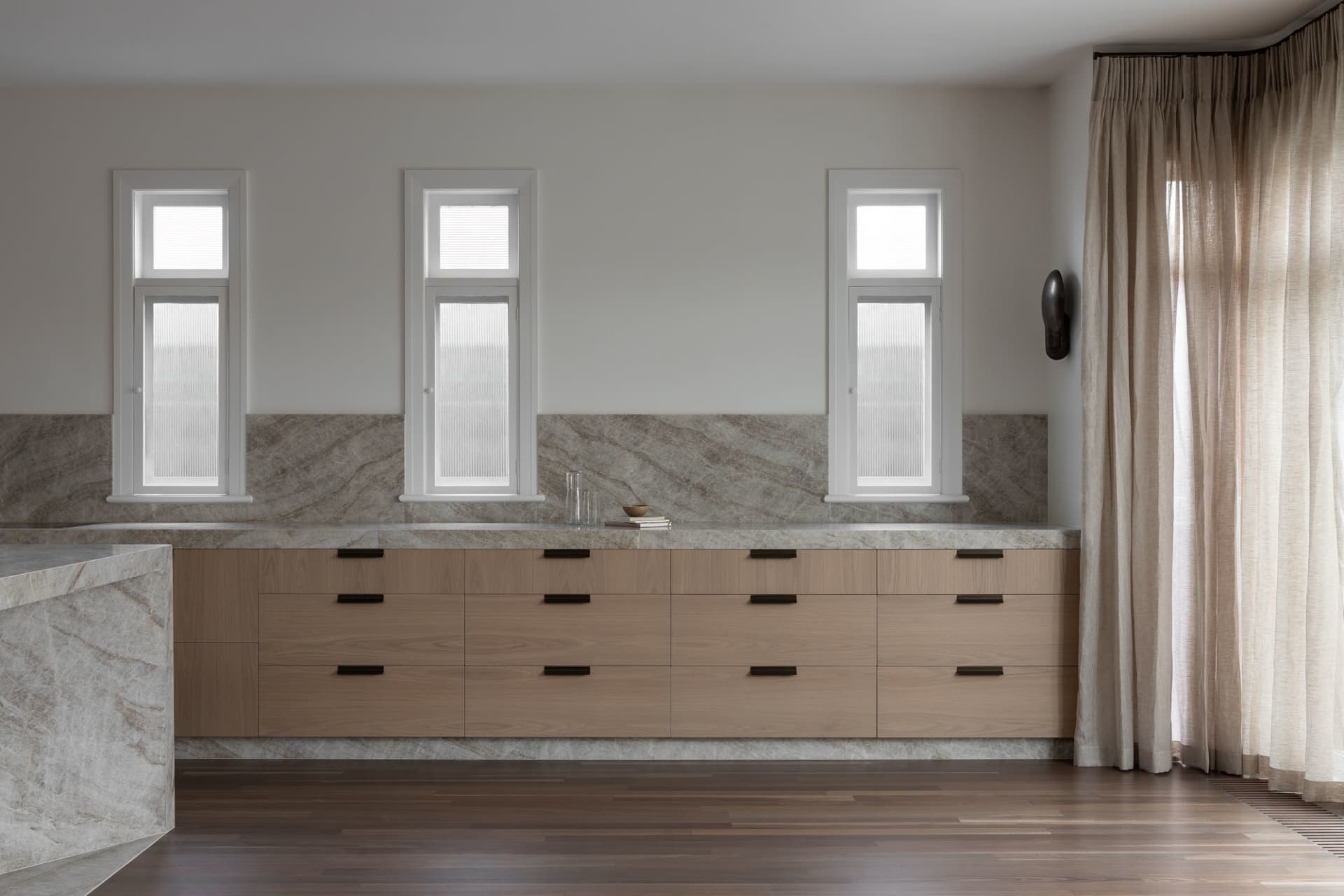 Modern minimalist kitchen with natural wood cabinets and marble countertop.