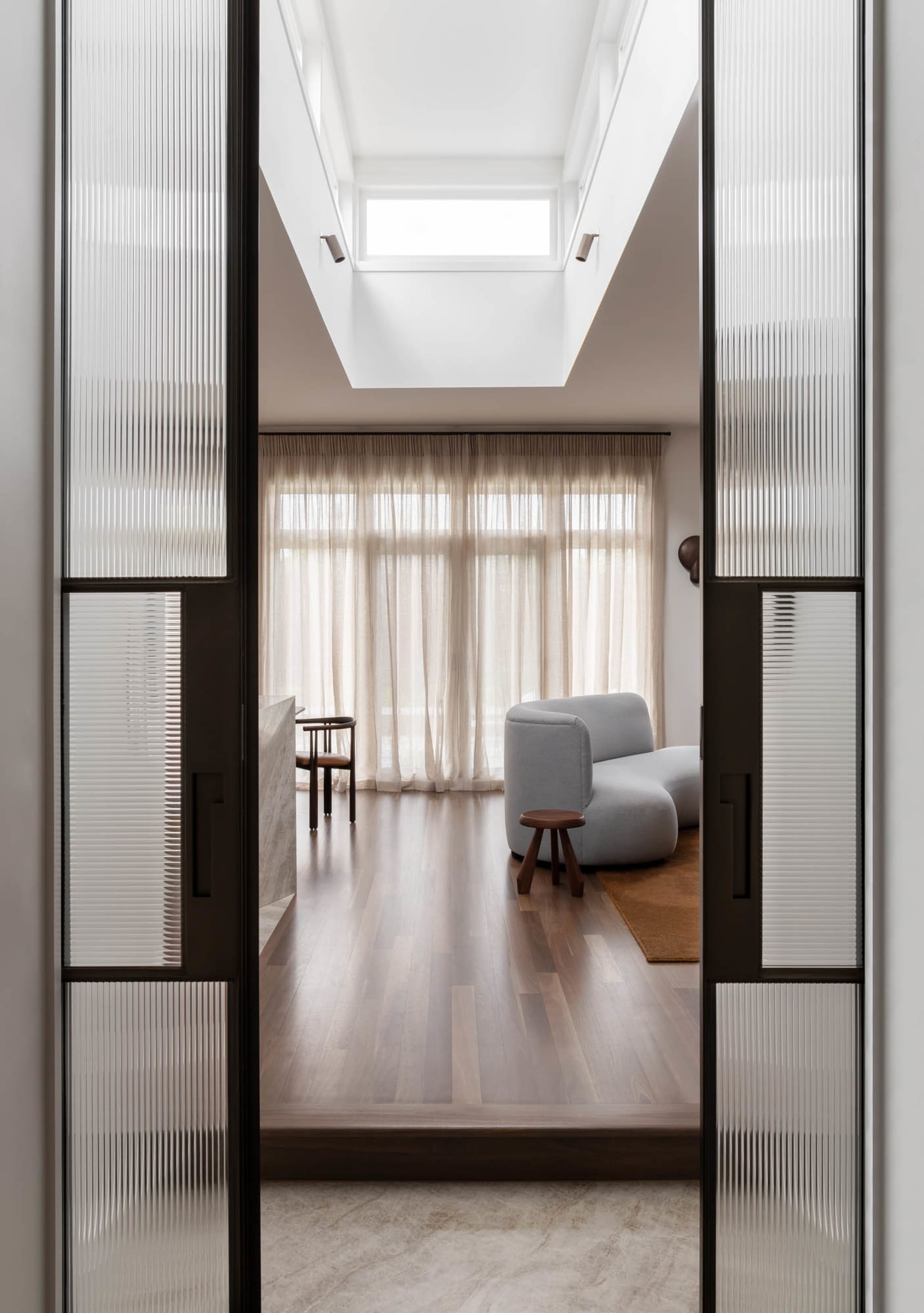 A modern minimalist living room featuring soft furnishings and wooden flooring.