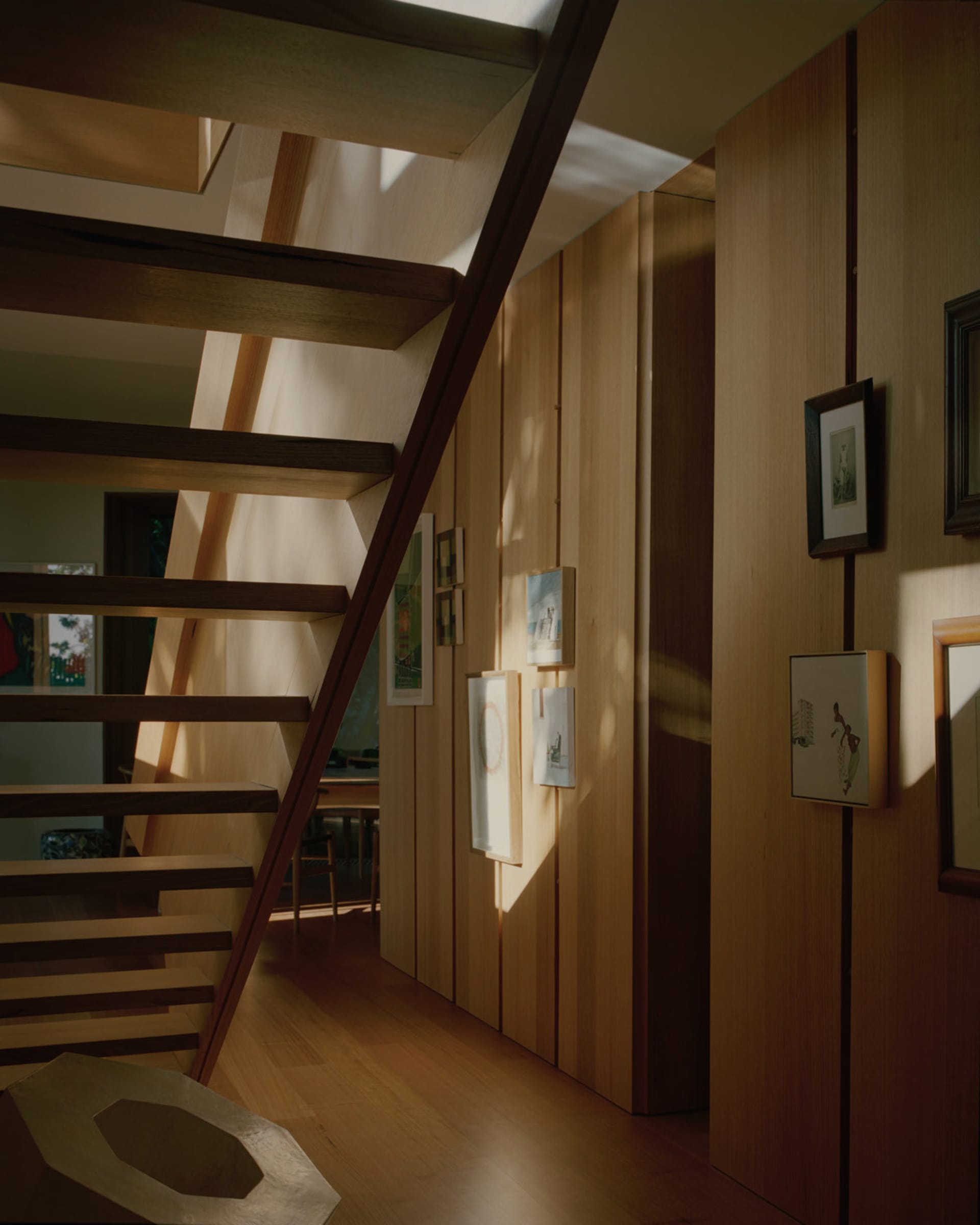 A modern staircase with wooden beams and framed artworks on the walls.