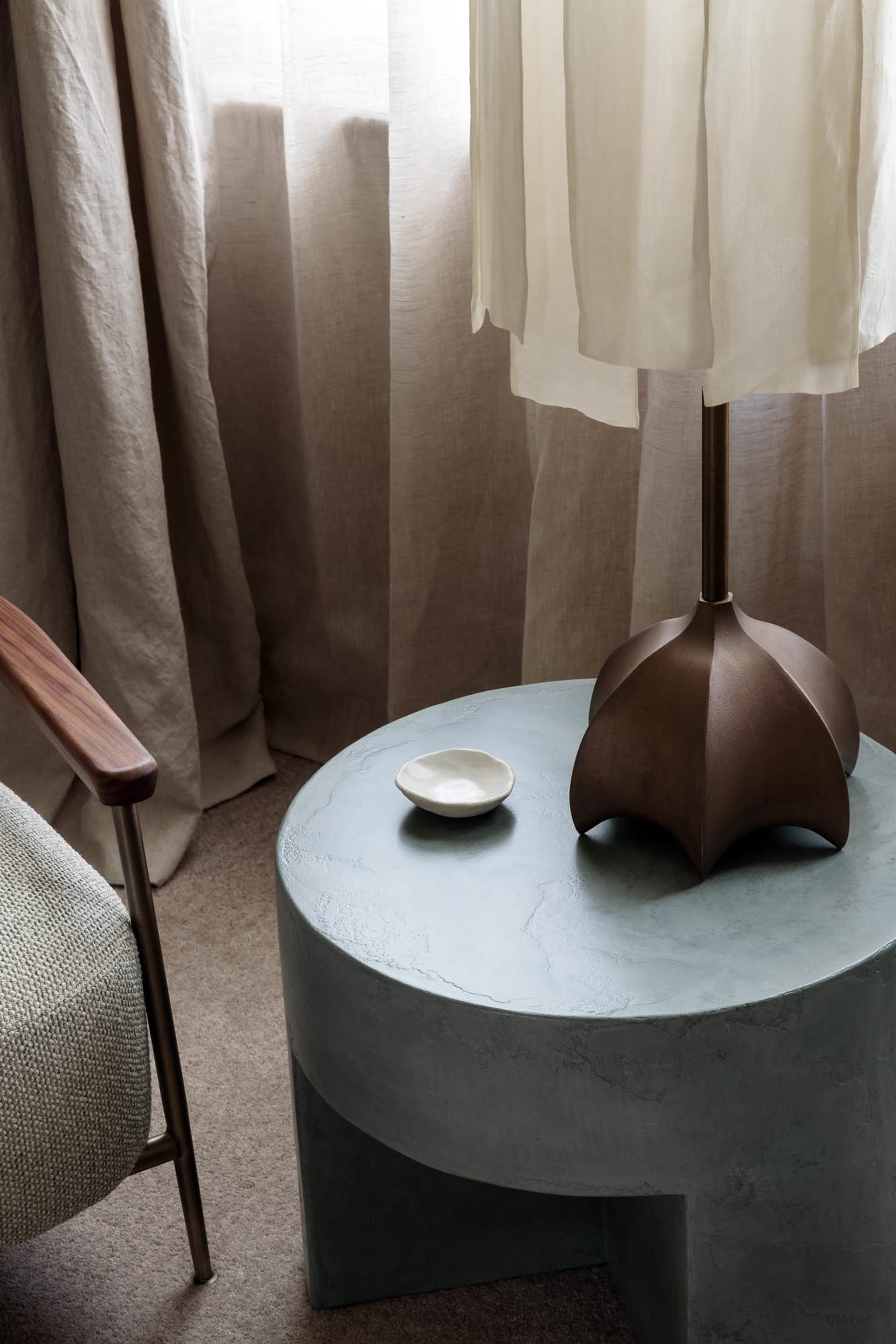 A modern concrete side table with a bronze lamp on it.