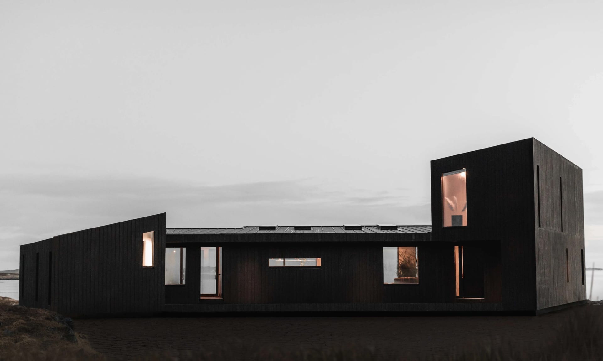 A modern house exterior with a minimalist design and black painted walls, featuring large windows and a simple geometric shap