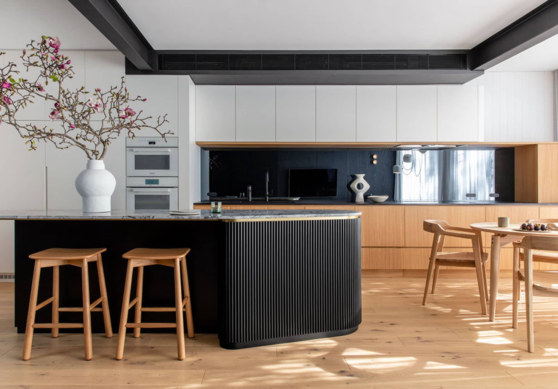 A modern minimalist kitchen with black and white color scheme, featuring a wooden island and marble countertops.