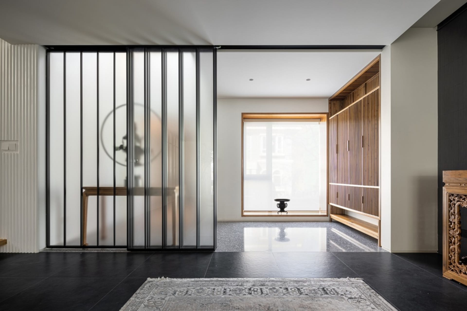Modern minimalist living room featuring glass sliding doors, wooden furniture, and stone flooring.