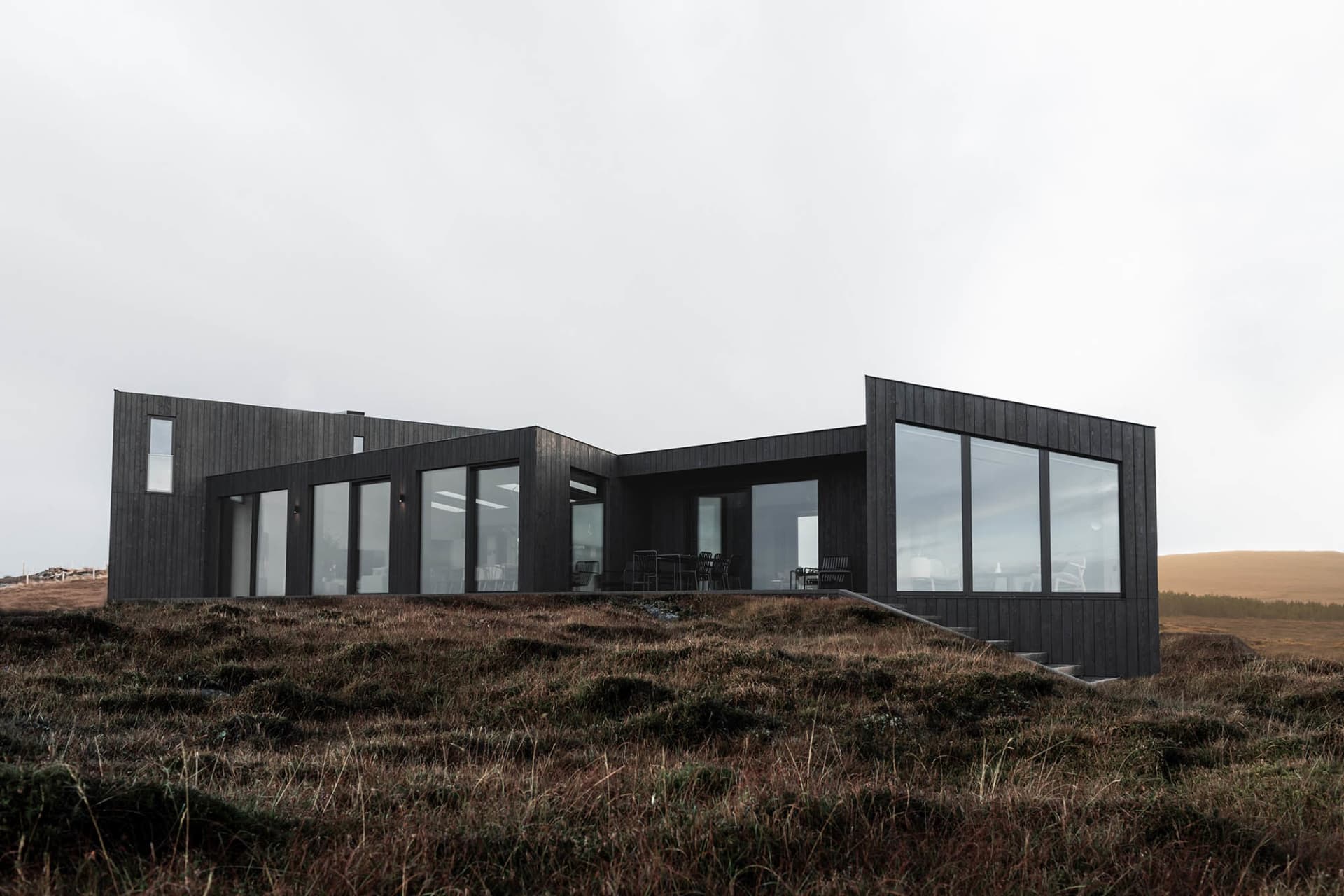Modern residential architecture featuring black wooden cladding on a grassy landscape.