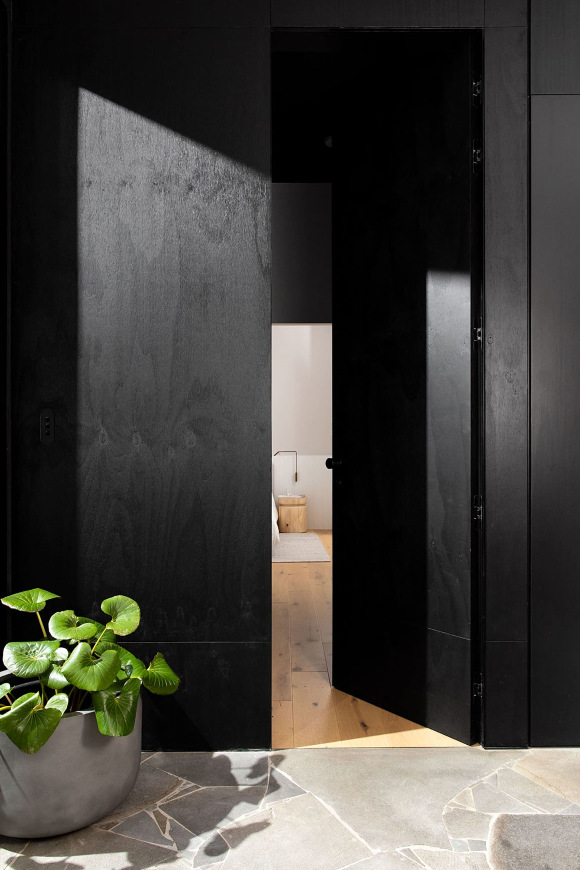 A modern interior with blackened wood walls and floor, featuring an open doorway leading to a bathroom.