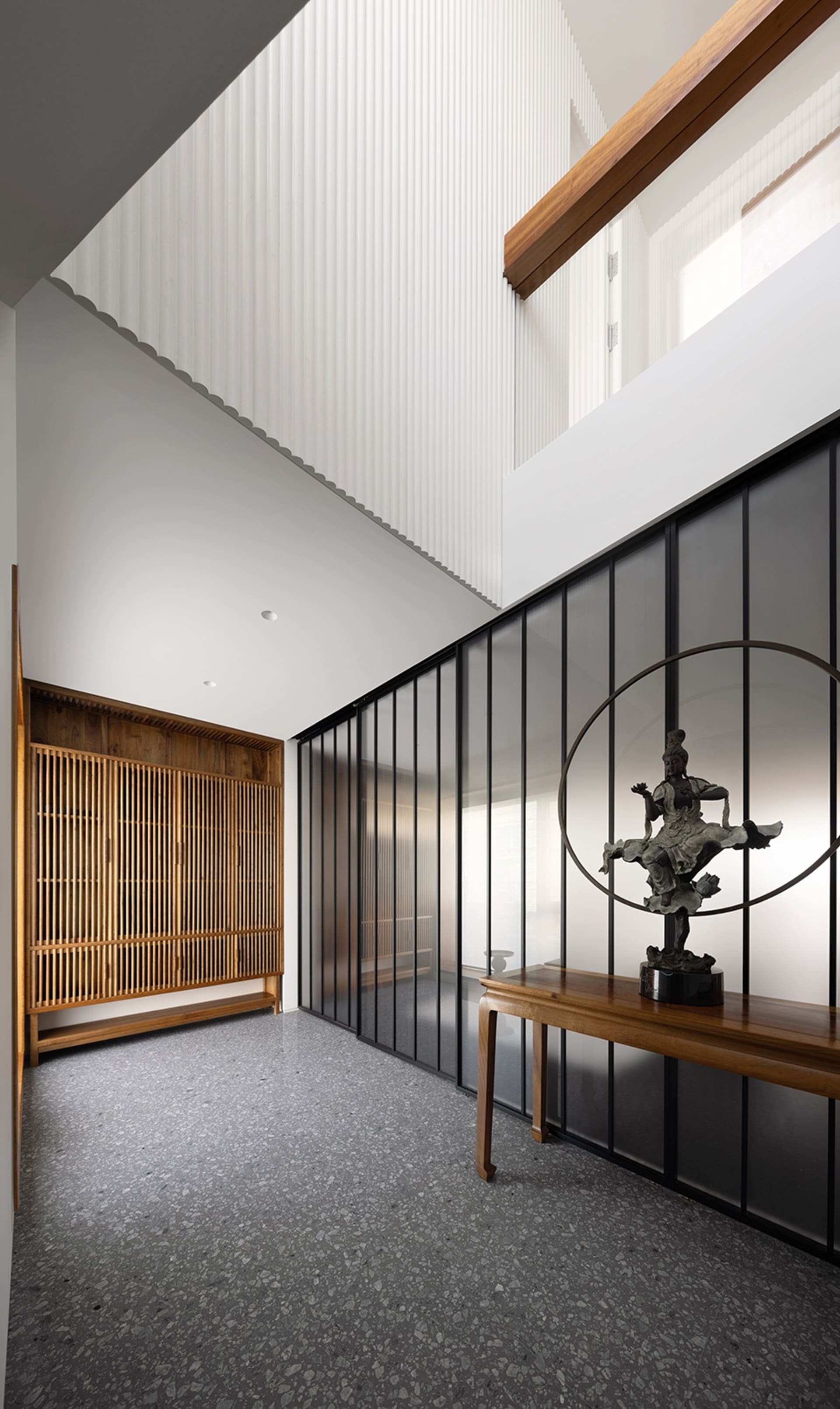 A modern interior entry hall with a wooden bench, glass walls, and a statue.