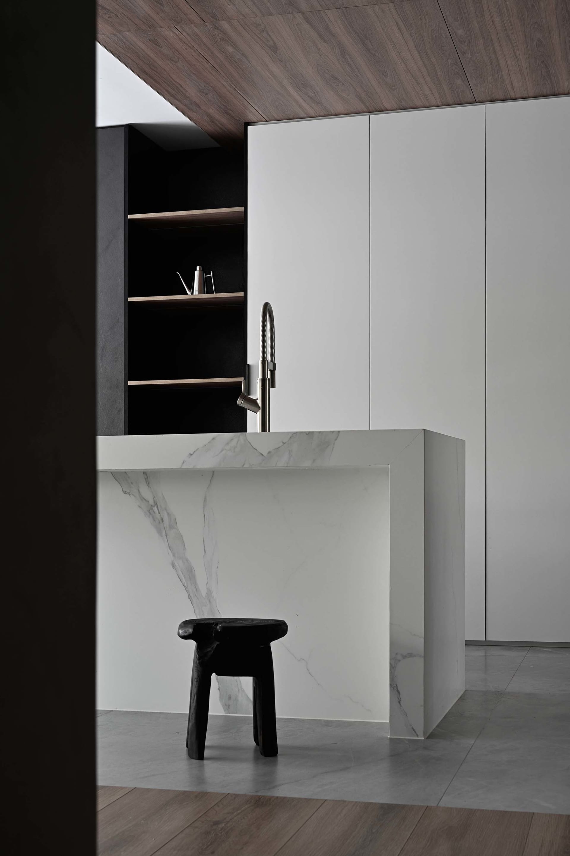 Modern minimalist kitchen with white marble countertops and black stools.