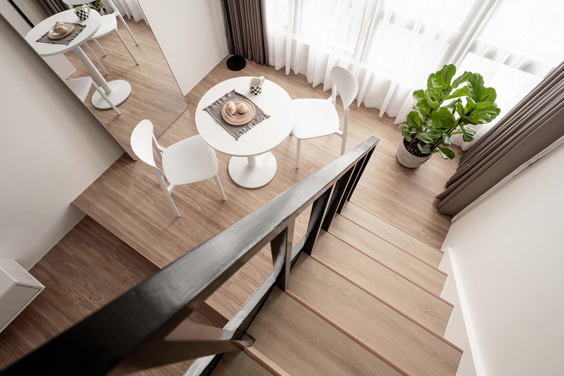 A minimalist dining area with white furniture, light wood flooring, and green plants.