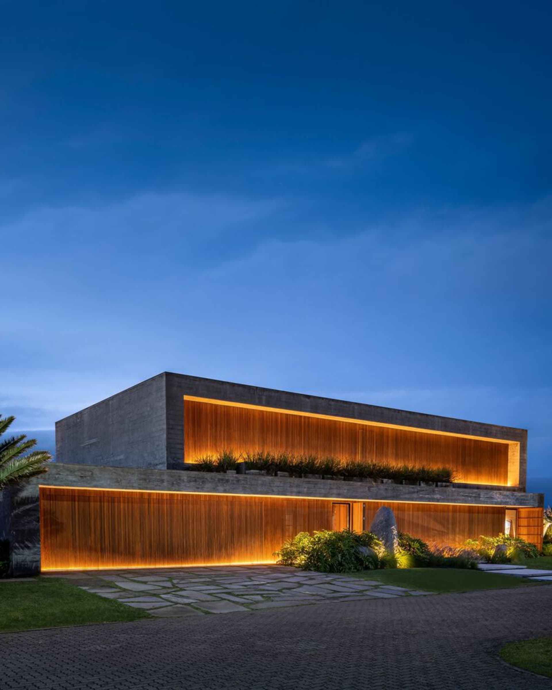 A modern minimalist house with concrete facade at night, illuminated by warm indoor lighting.