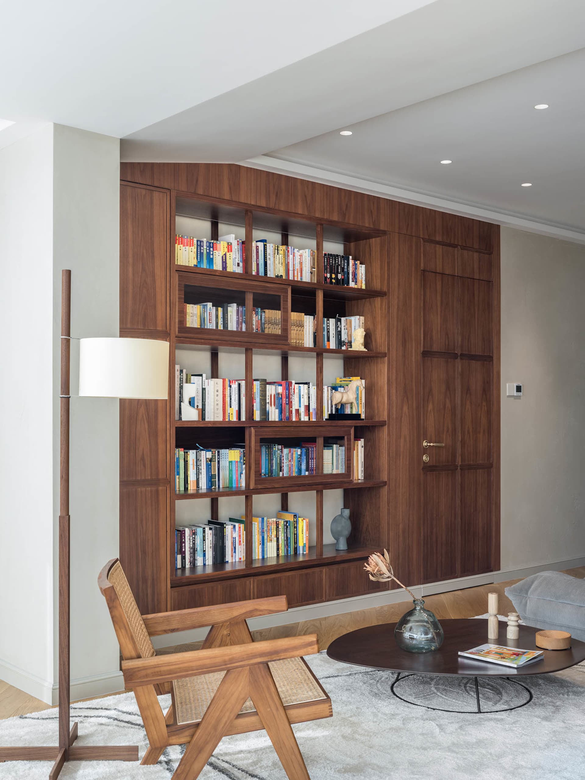 A living room with industrial-style decor, featuring wooden shelves filled with books and a wooden armchair on a rug.