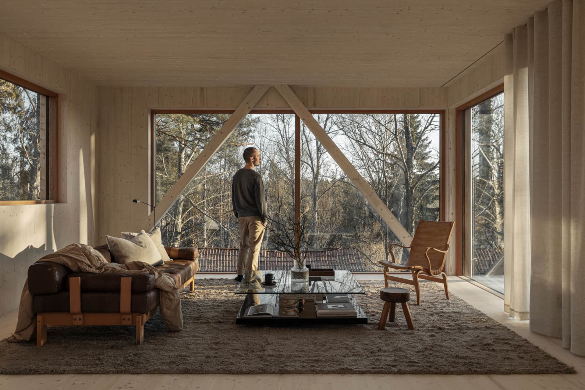A minimalist living room with wooden beams and large windows showcasing a forest view.