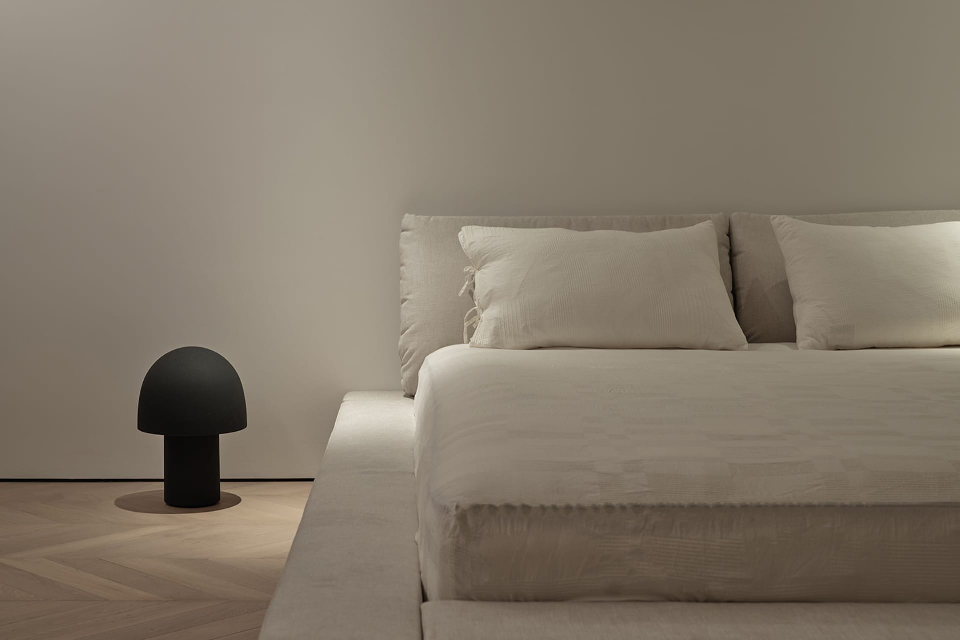 A minimalist white bedroom featuring a fabric bed with a simple, elegant headboard and side table.