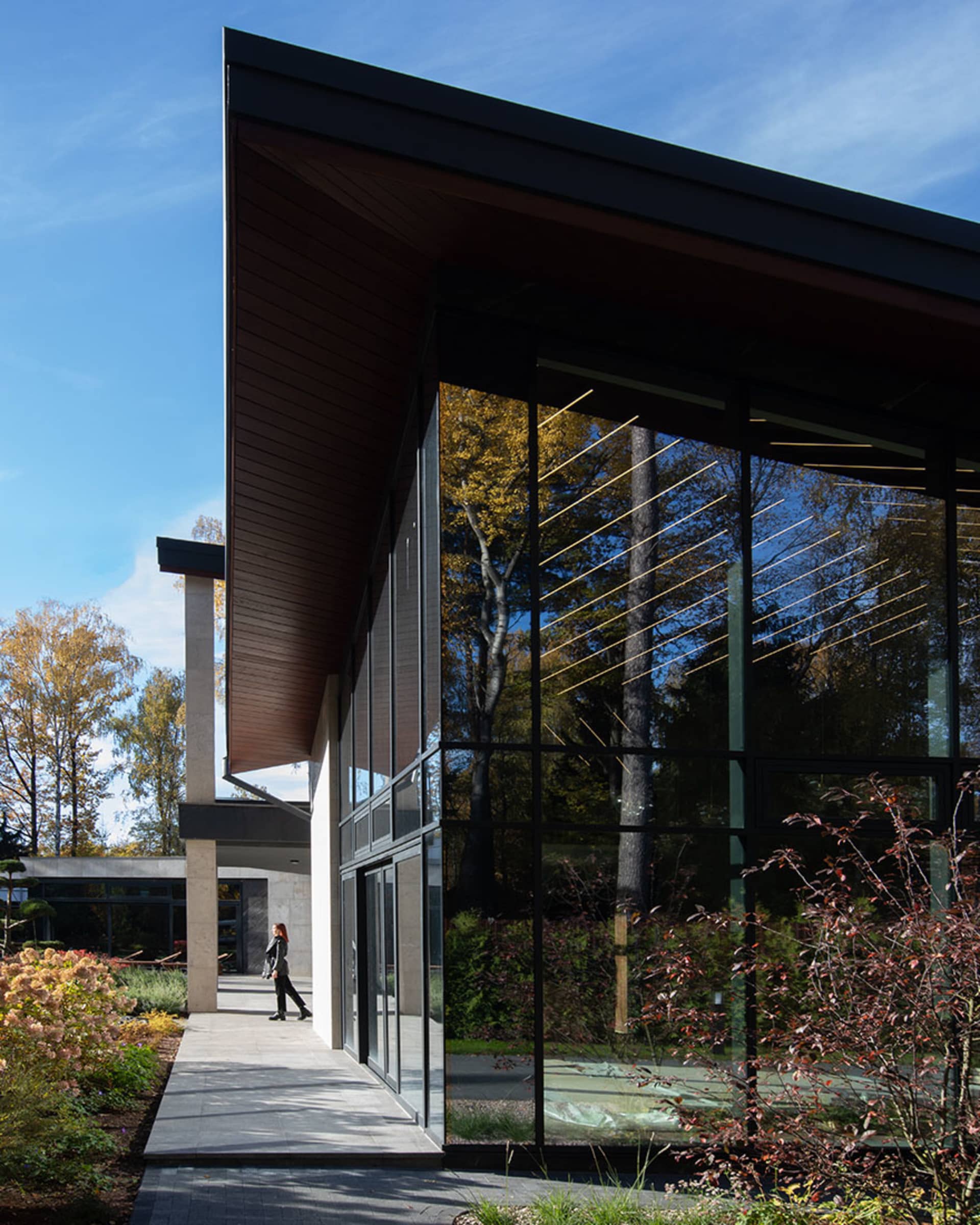 Modern building with large glass windows and a concrete base, surrounded by greenery and clear blue sky.