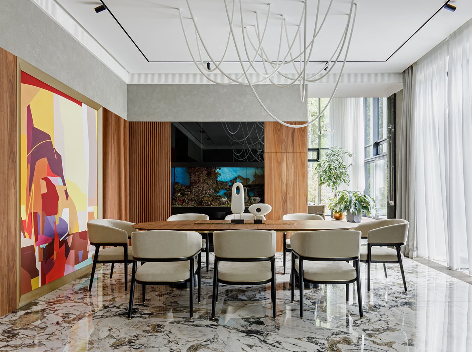 Modern dining room featuring a wooden dining table with marble top, surrounded by white cushioned chairs and a large colorful