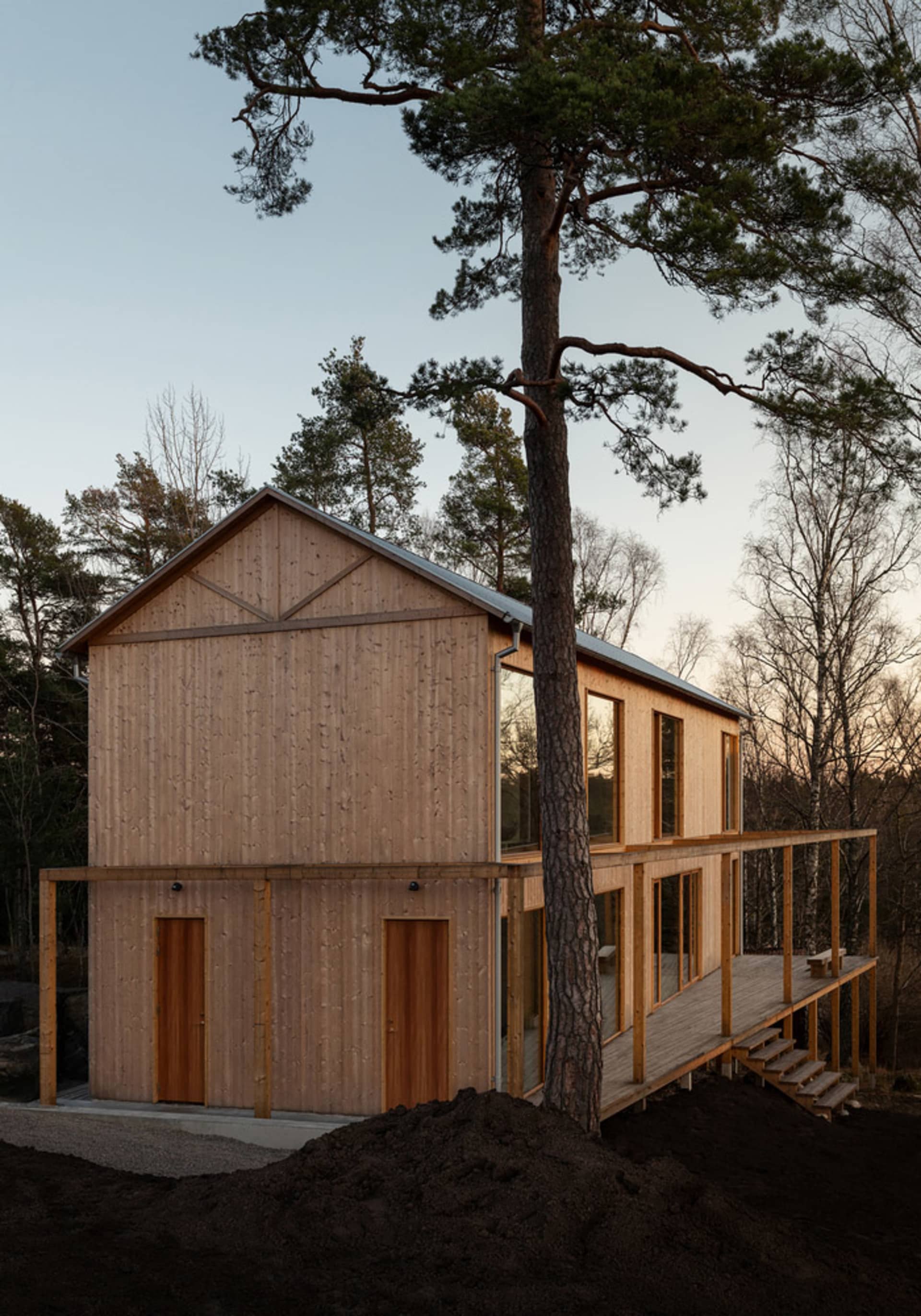 Modern house exterior with wooden siding and large windows surrounded by trees.