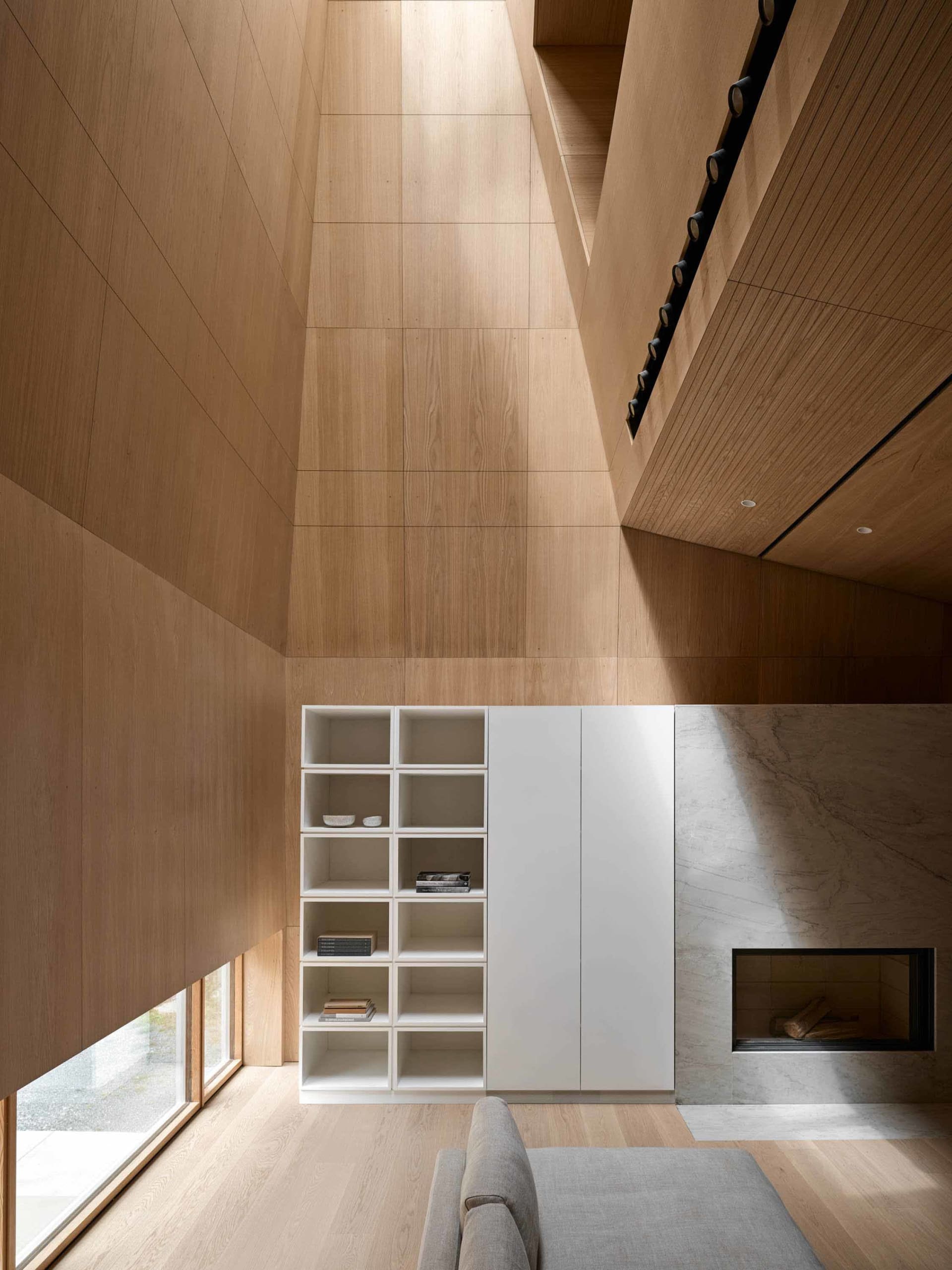 A modern living room interior with wooden walls, ceiling, and floor, featuring a minimalist shelf system and a sleek fireplac