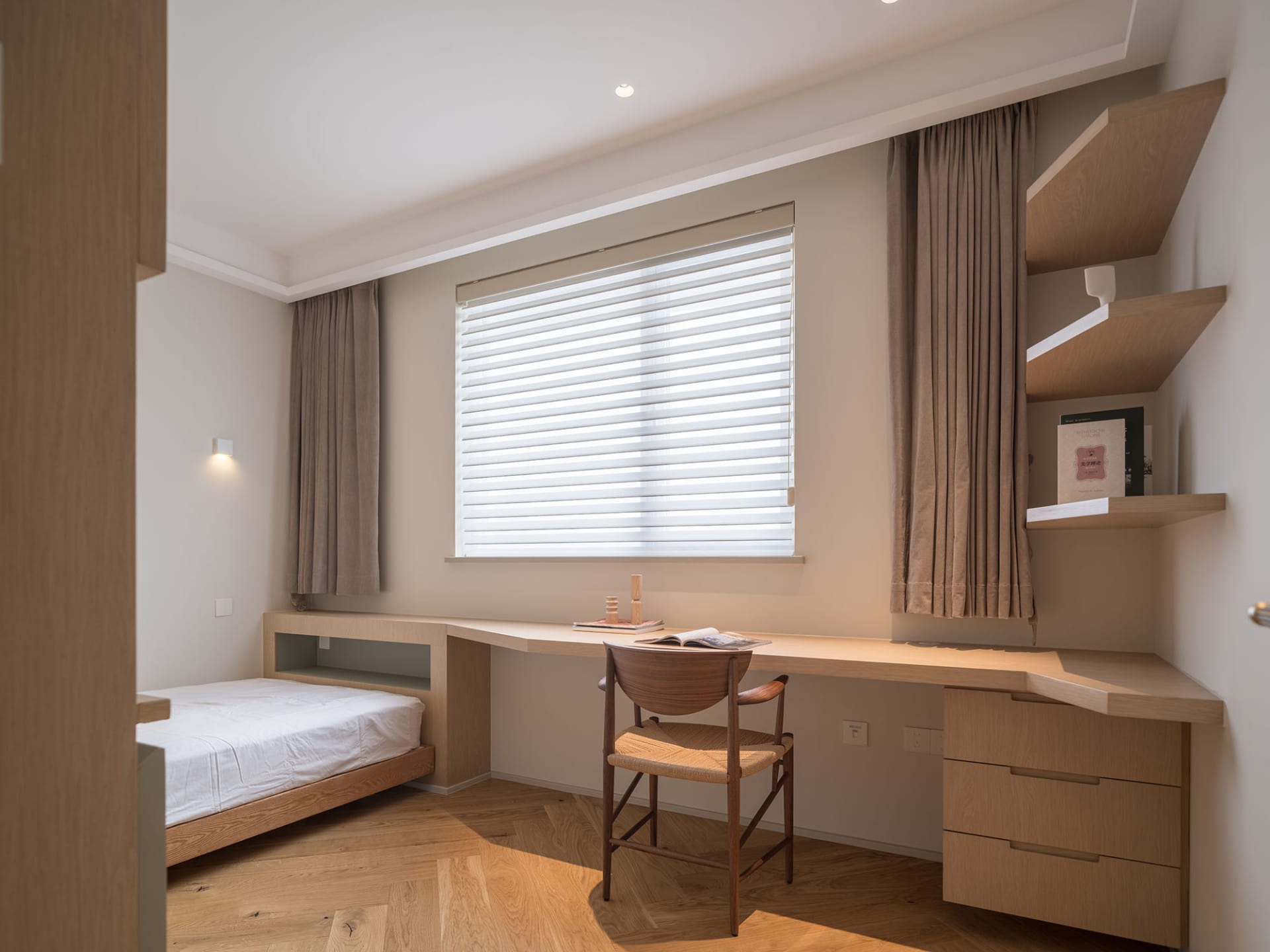 A minimalist bedroom featuring modern furniture made of wood, with a bed, desk, and shelves.