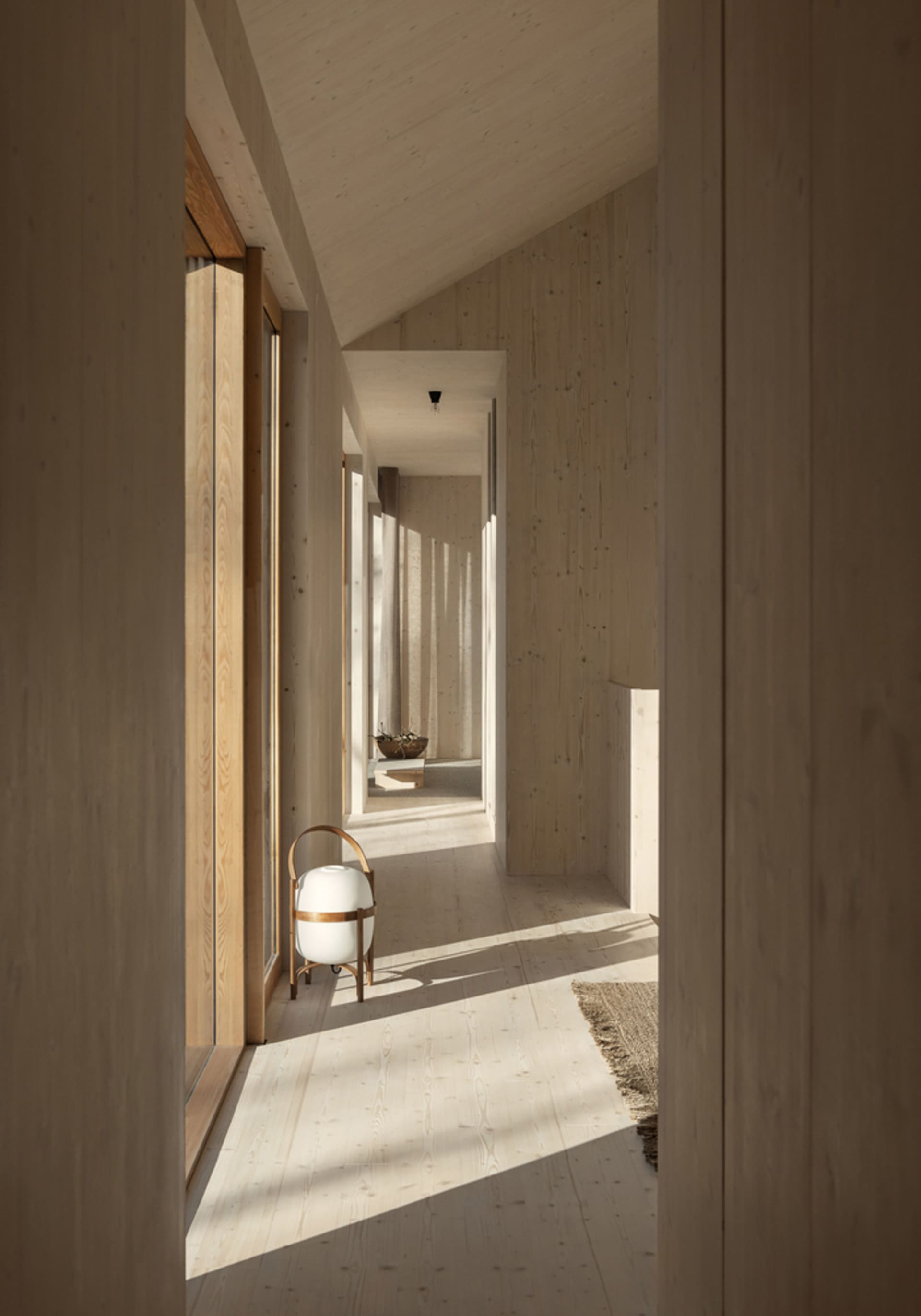 A minimalist modern hallway with wooden walls and flooring, featuring a white spherical lamp and a natural light atmosphere.