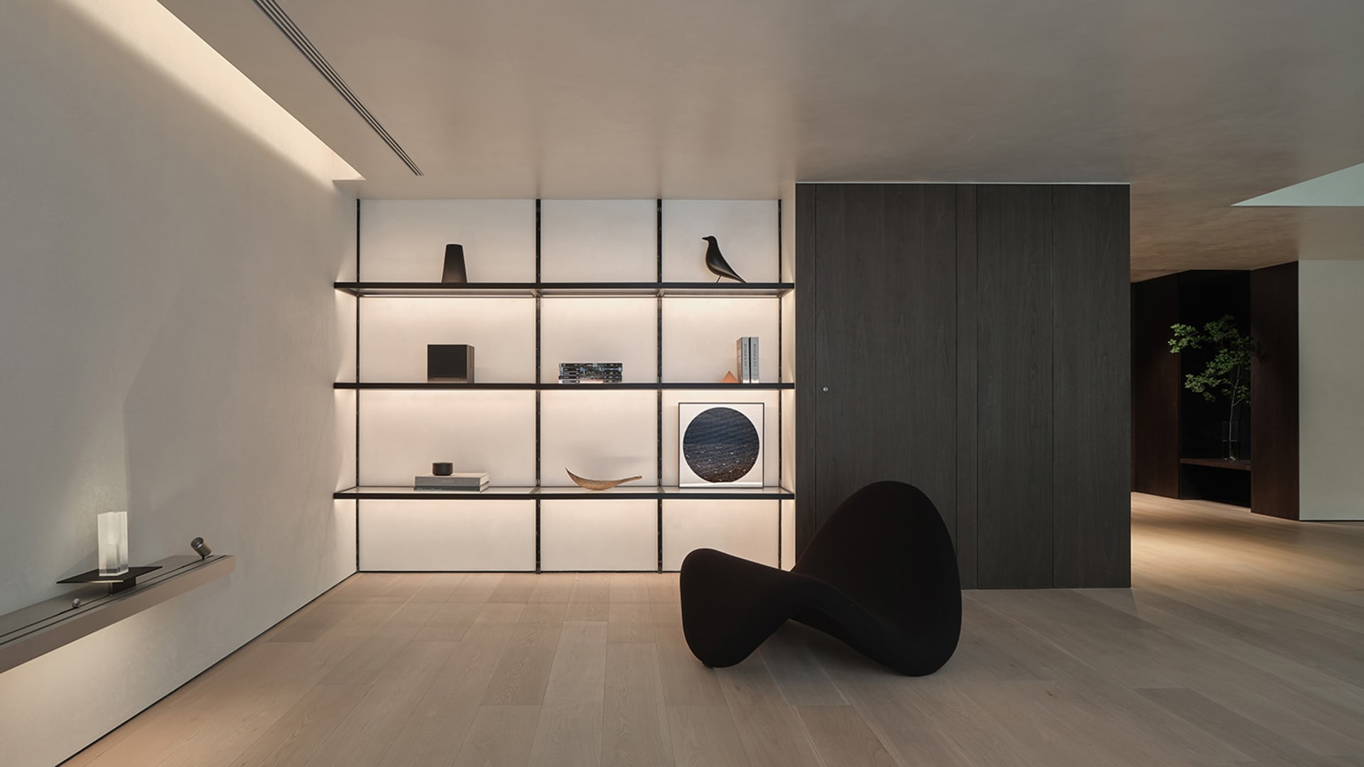 A minimalist living room featuring modern metal shelving with a single black sculptural chair, illuminated by hidden lighting