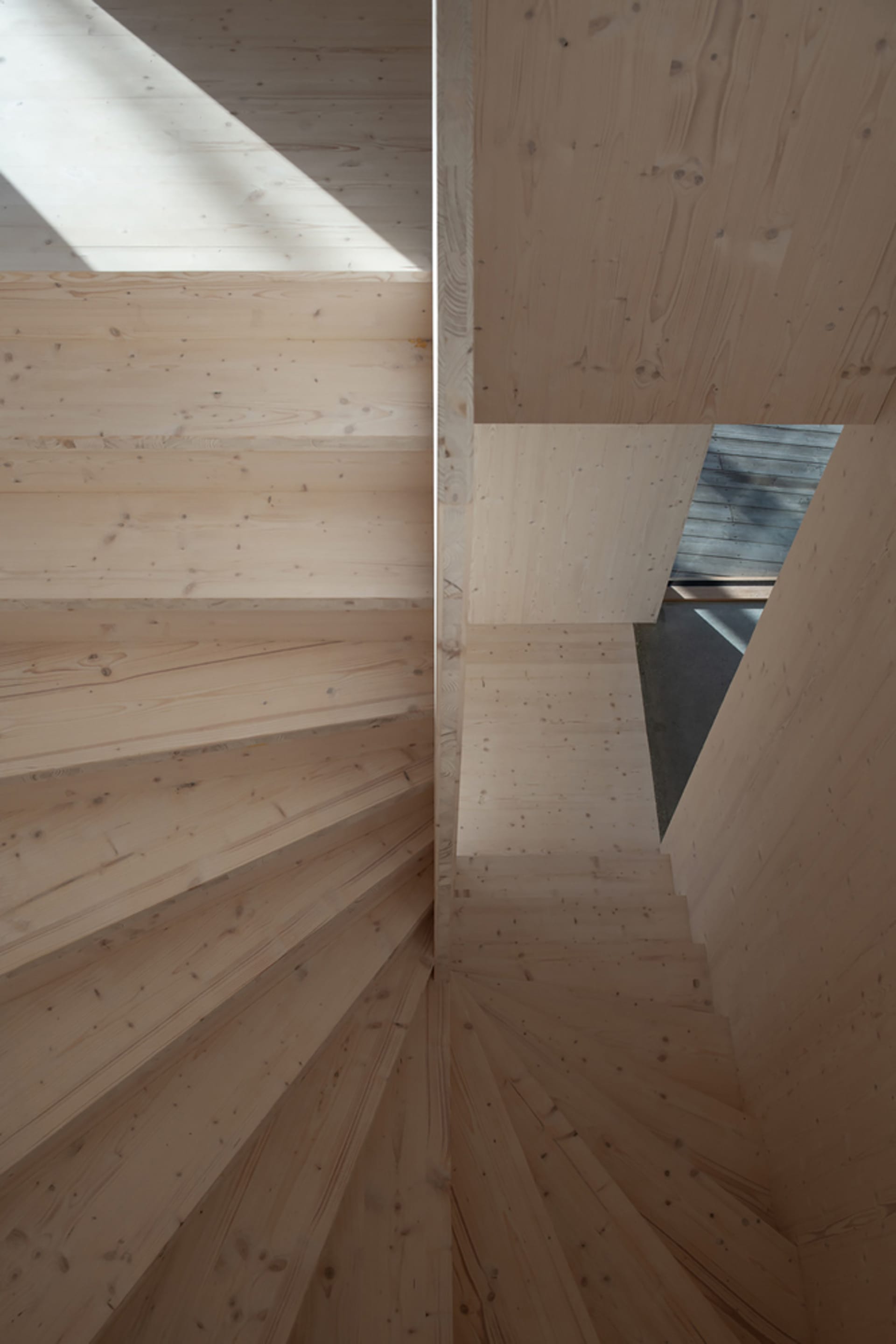 A modern, wooden staircase with a geometric design and natural light coming through a skylight.