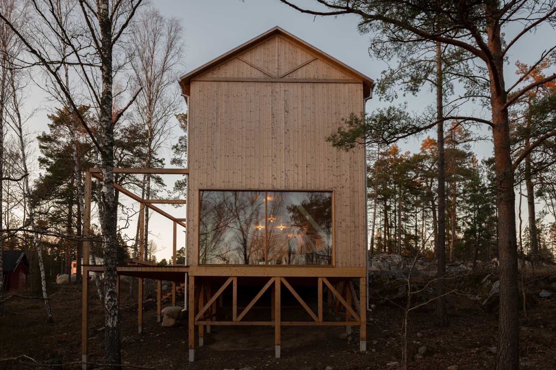 Modern minimalist wooden house surrounded by trees with a large window.