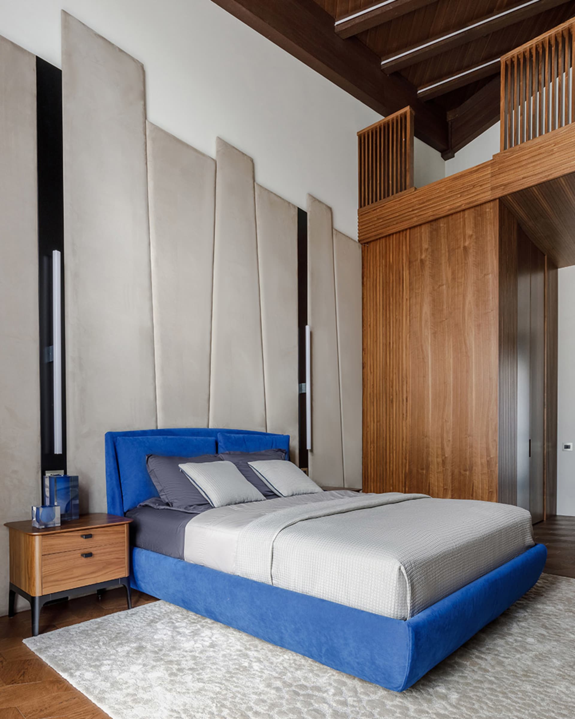 A modern bedroom featuring a blue velvet bed and wooden acoustic panels.