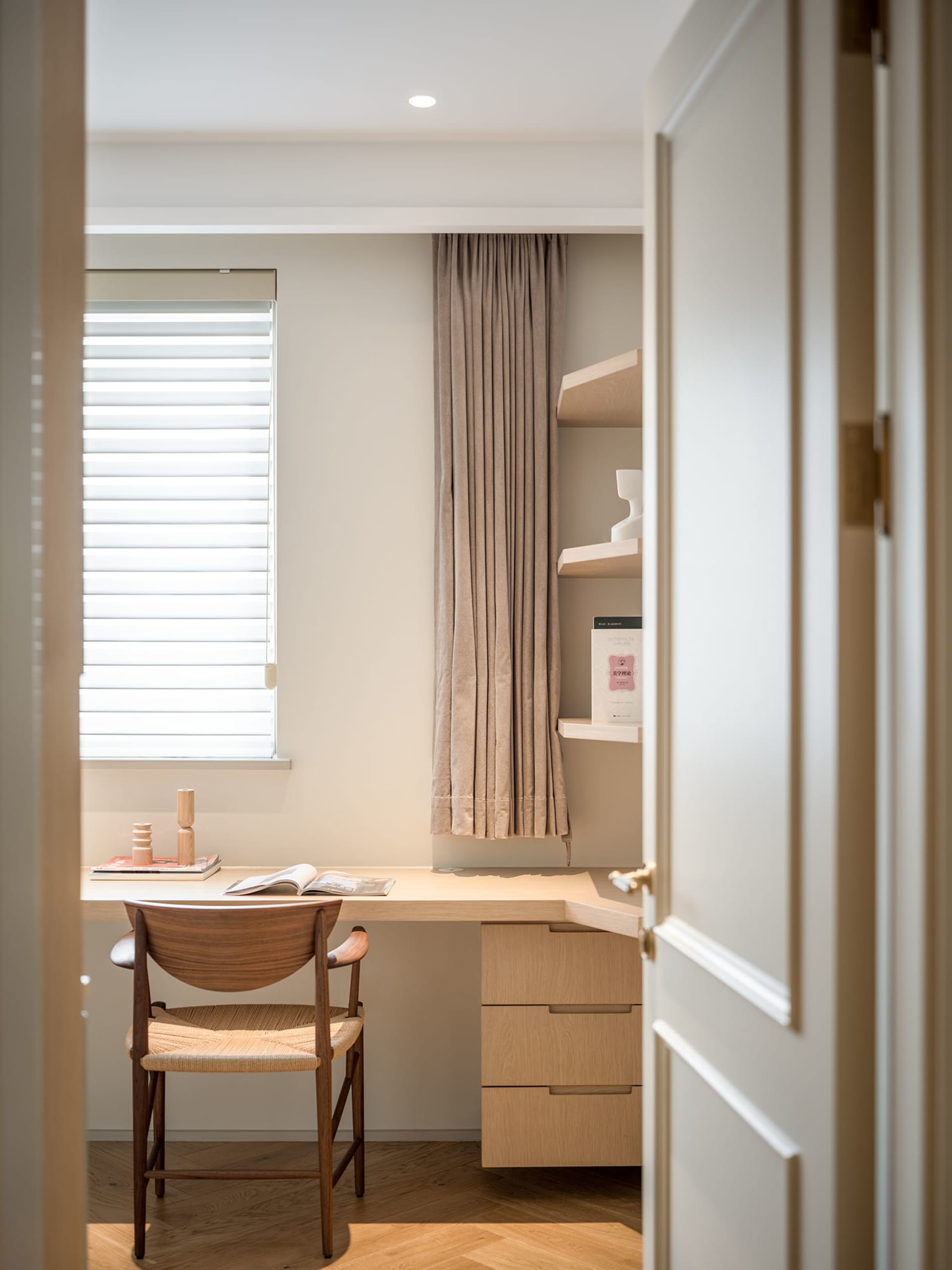 A modern home office featuring wooden furniture, a window with blinds, and a bookshelf.