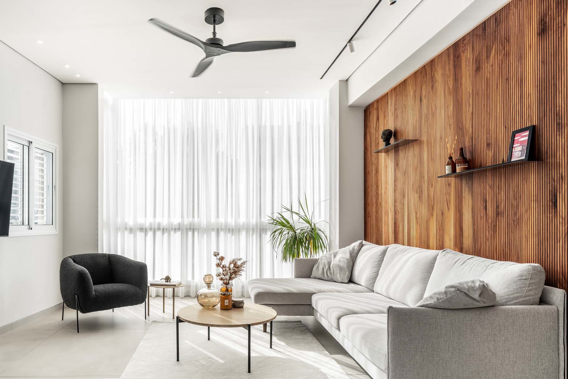 A modern living room featuring wood-paneled walls, a concrete floor, and a comfortable grey sofa with white cushions, illumin