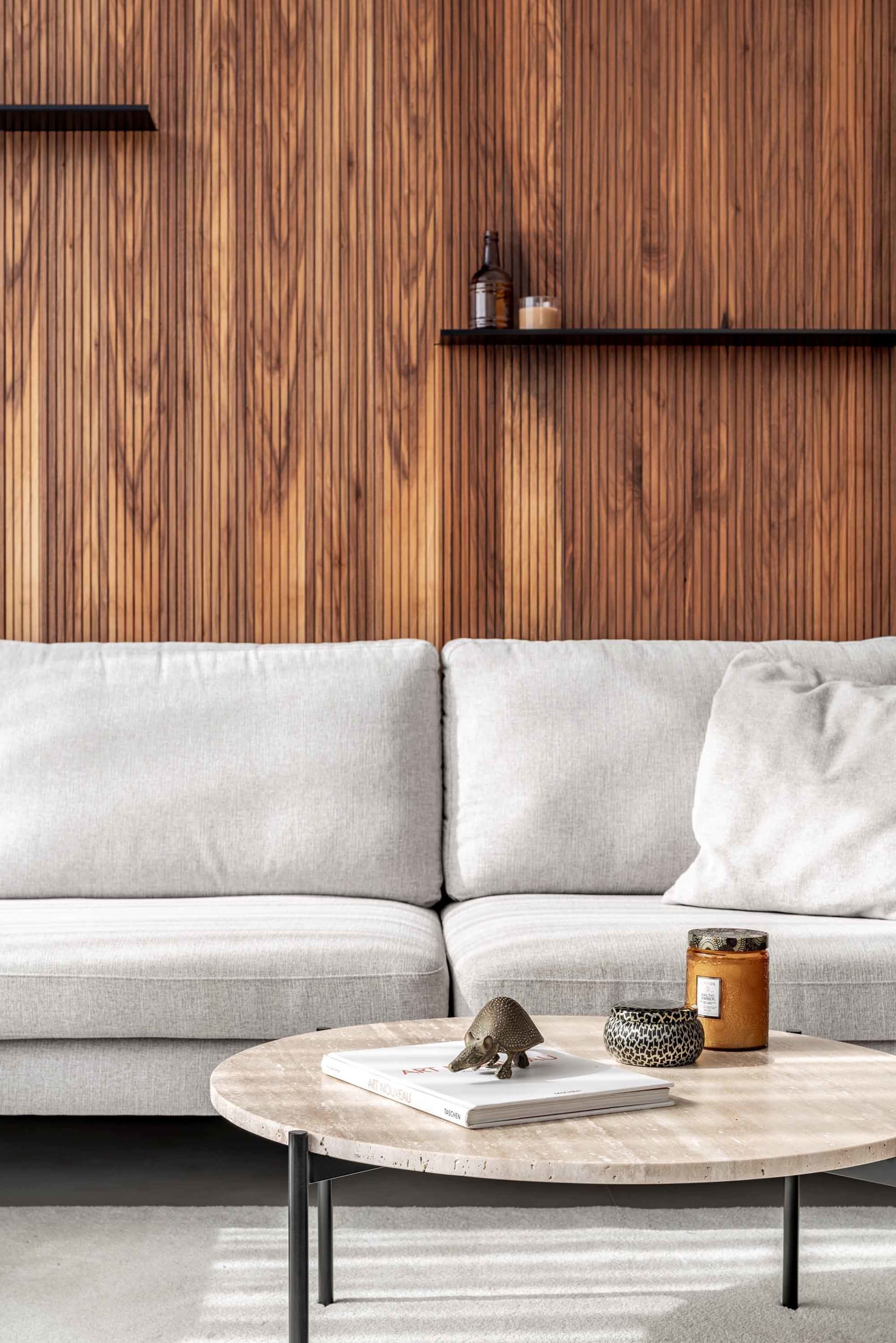 A modern living room with a white couch, wooden paneling, and a coffee table with decorative items.