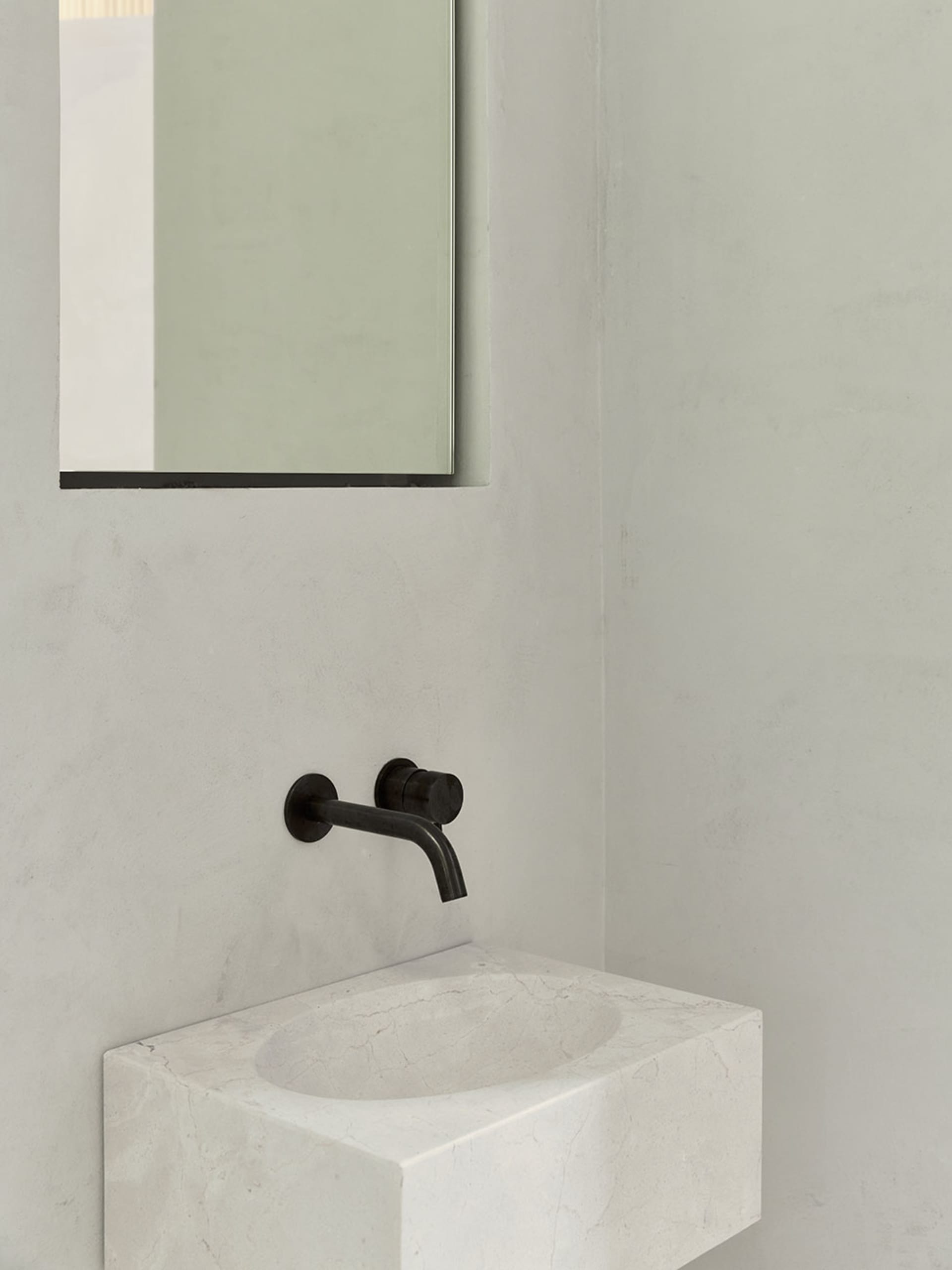 Modern bathroom featuring a minimalist white marble sink with a black faucet and a rectangular mirror on the wall.