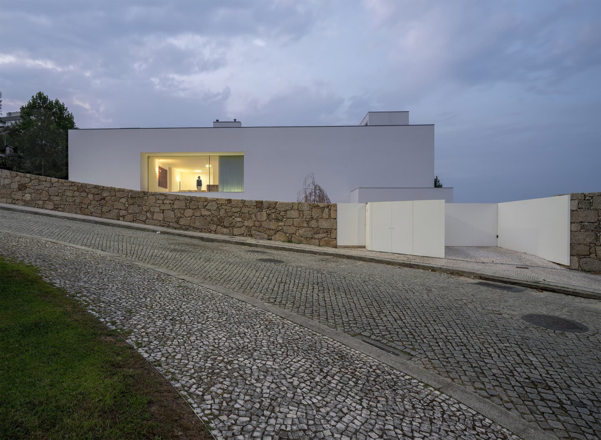 Modern residential exterior with a white stone wall and large glass windows.