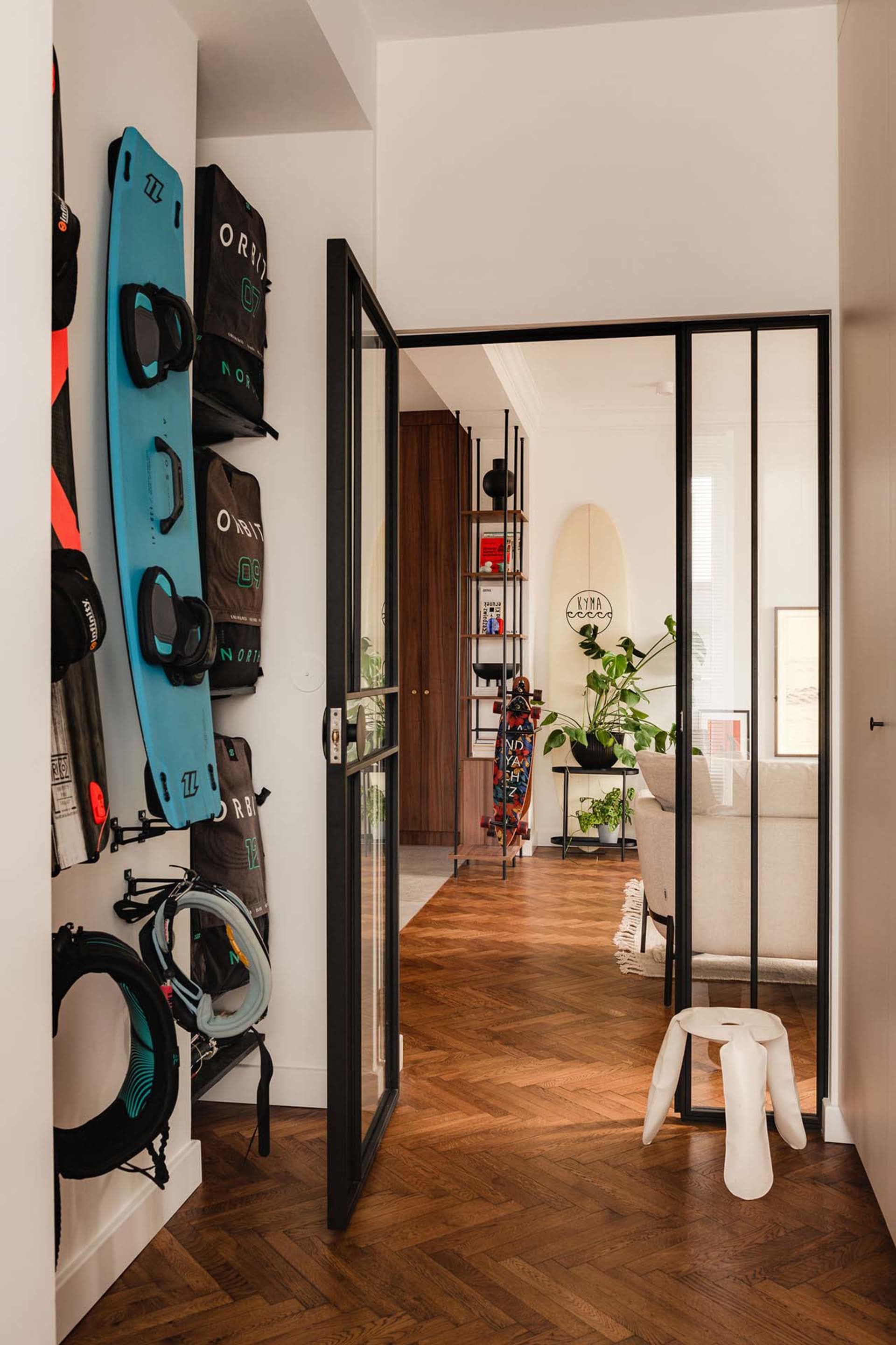 A modern residential interior with parquet flooring, glass doors, and wooden trim features skateboards and a living room area