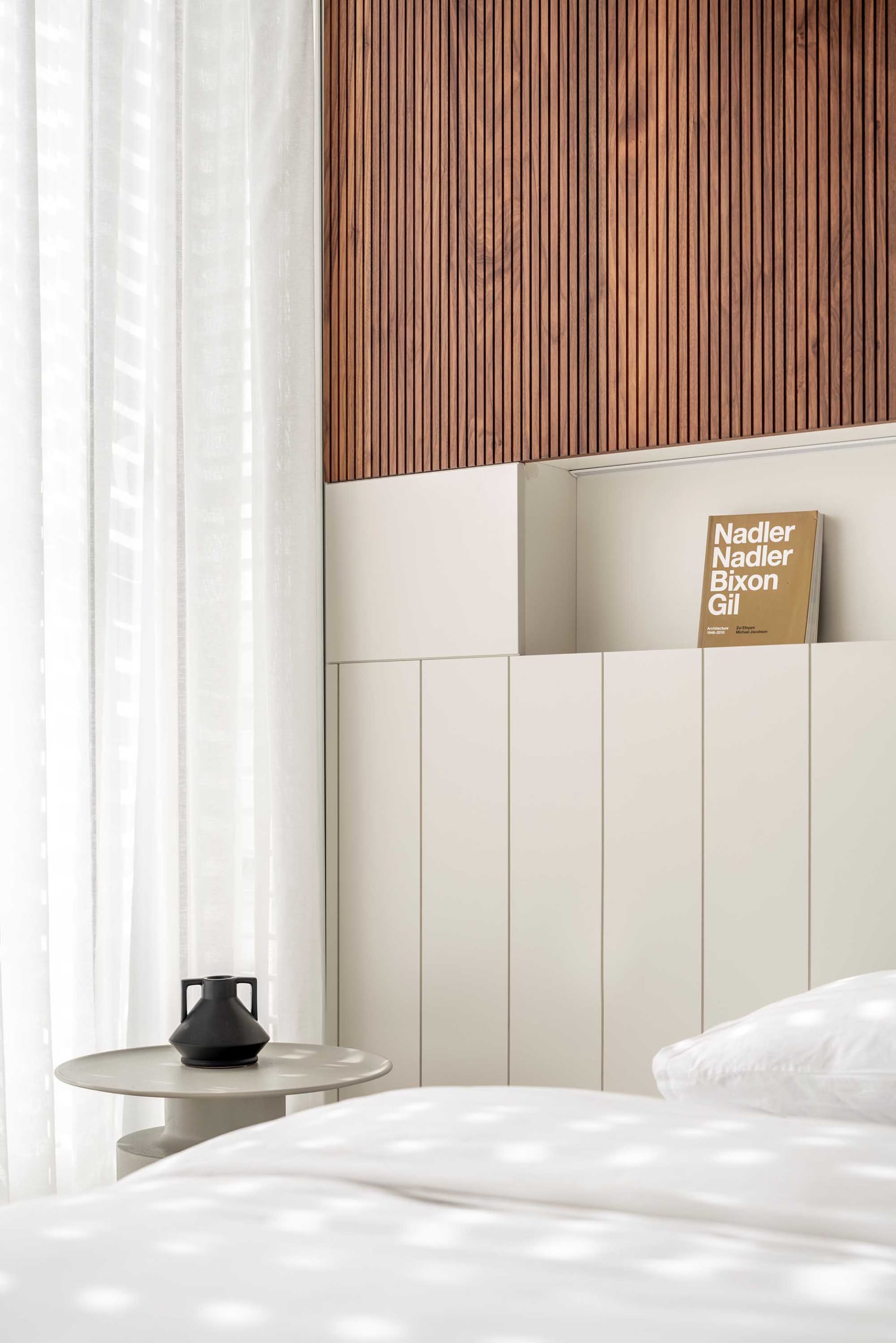 Minimalist bedroom featuring a wooden headboard, white curtains, and a white bed.
