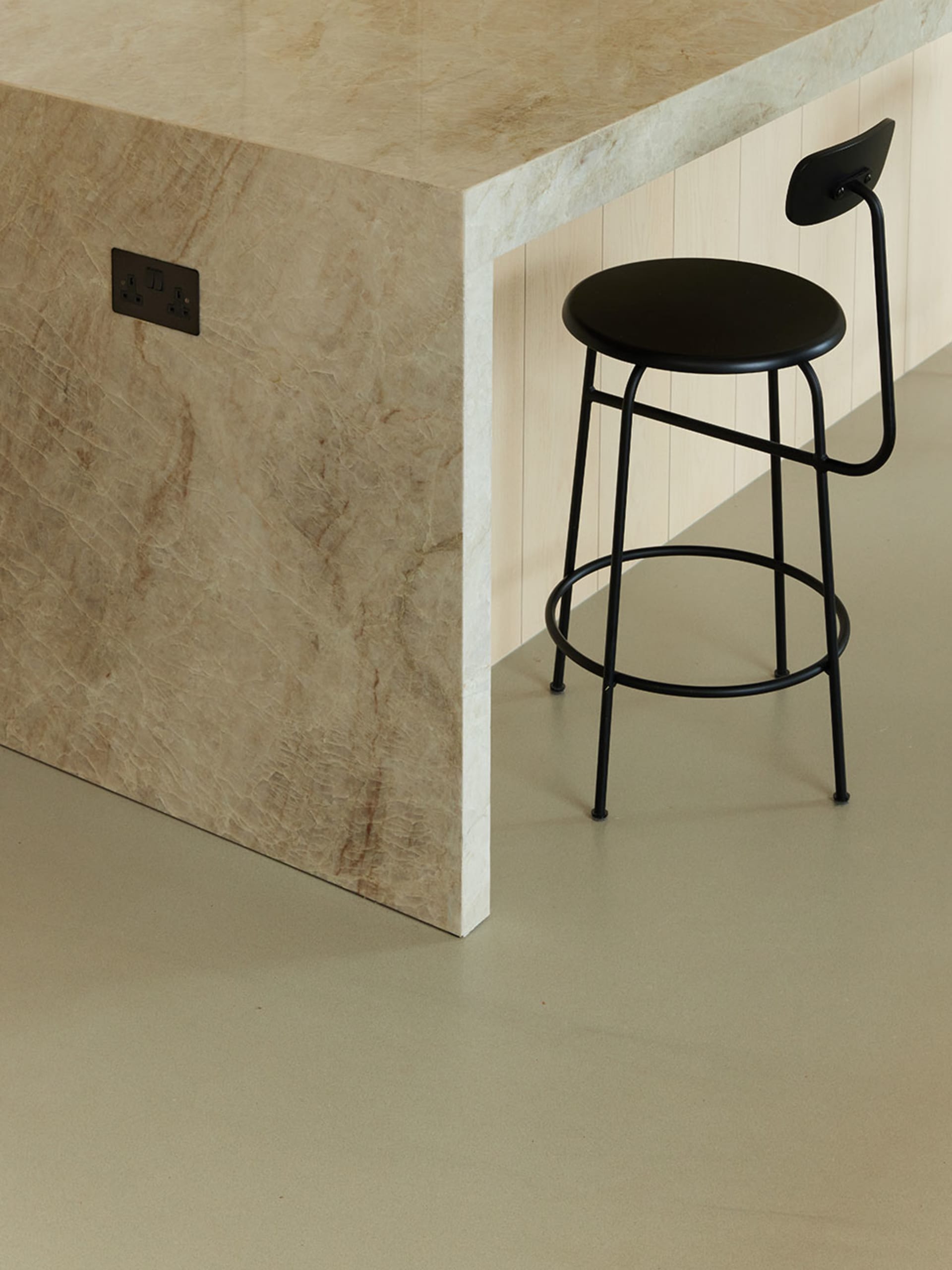Modern kitchen counter with a marble surface and a black stool next to it.