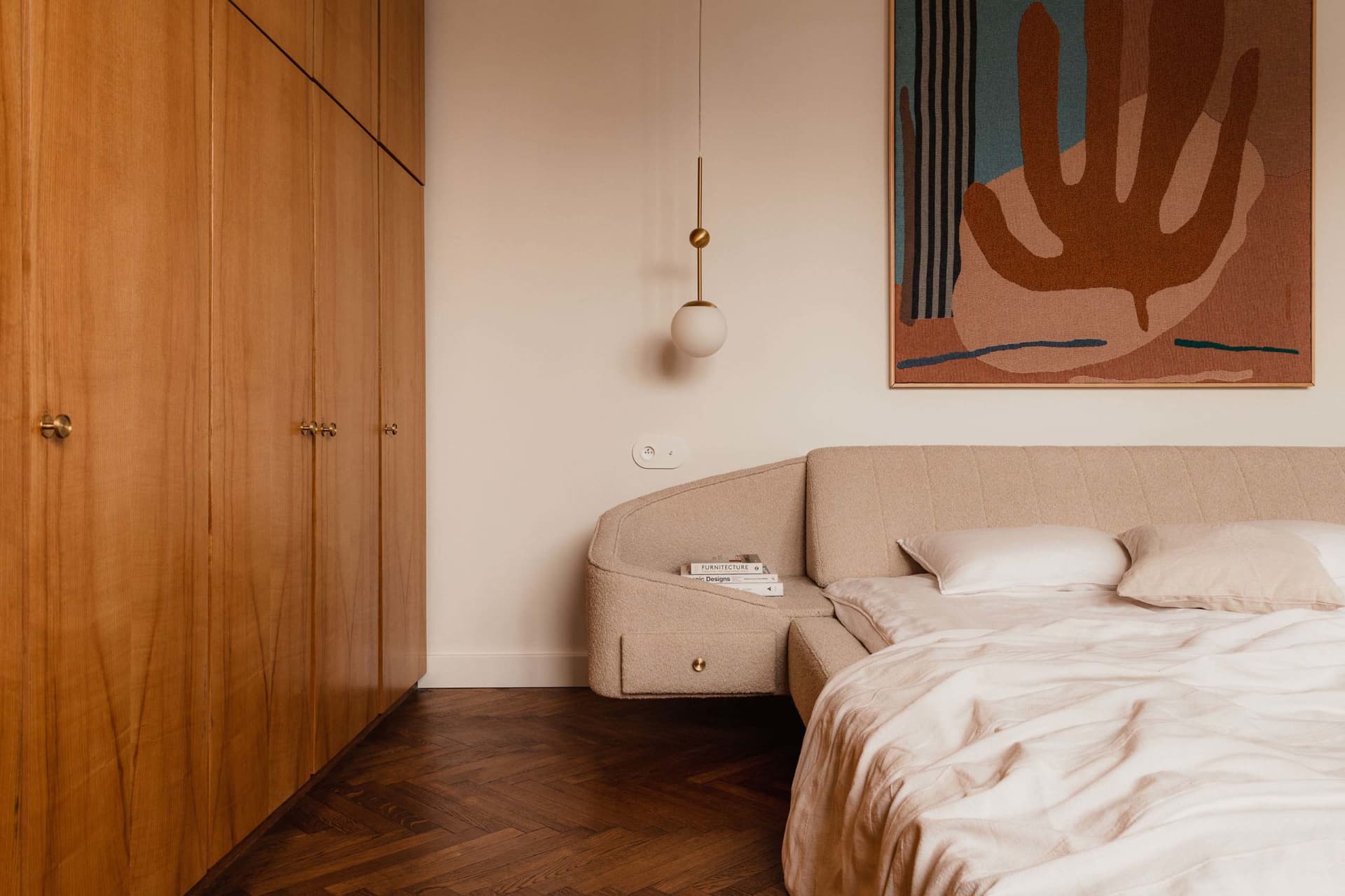 A modern bedroom featuring a beige sofa with a textured fabric, set against a warm wooden floor and a minimalist wall with a