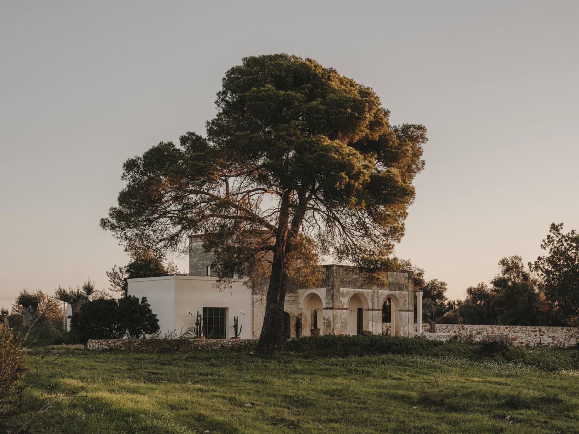 Modern residential exterior featuring a concrete house with stone accents and a lush green landscape.