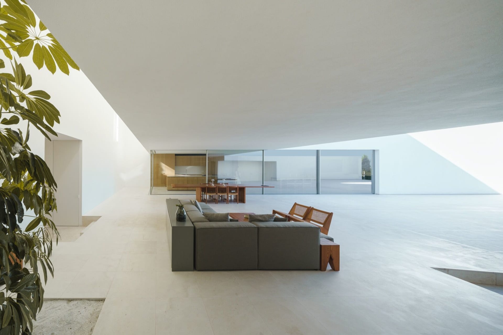 Modern living room with concrete floor and minimalist furniture, glass doors, and large windows.